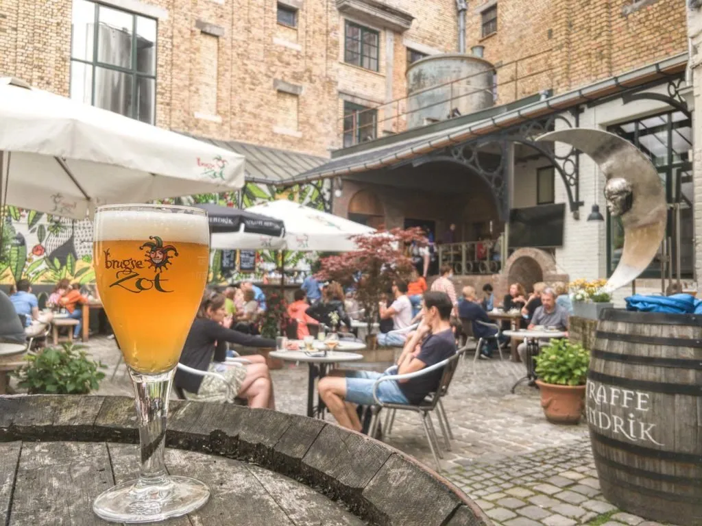 The courtyard at De Halve Maan brewery in Bruges, with a Brugse Zot beer in a glass on a barrel table and a Straffe Hendrik cask alongside