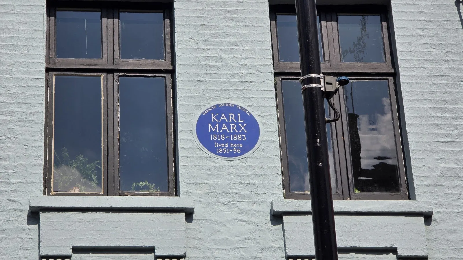 The round blue Greater London Council plaque to Karl Marx, 1818–1883, "lived here 1851–56", between two tall black-framed windows on the pale grey front of 28 Dean Street
