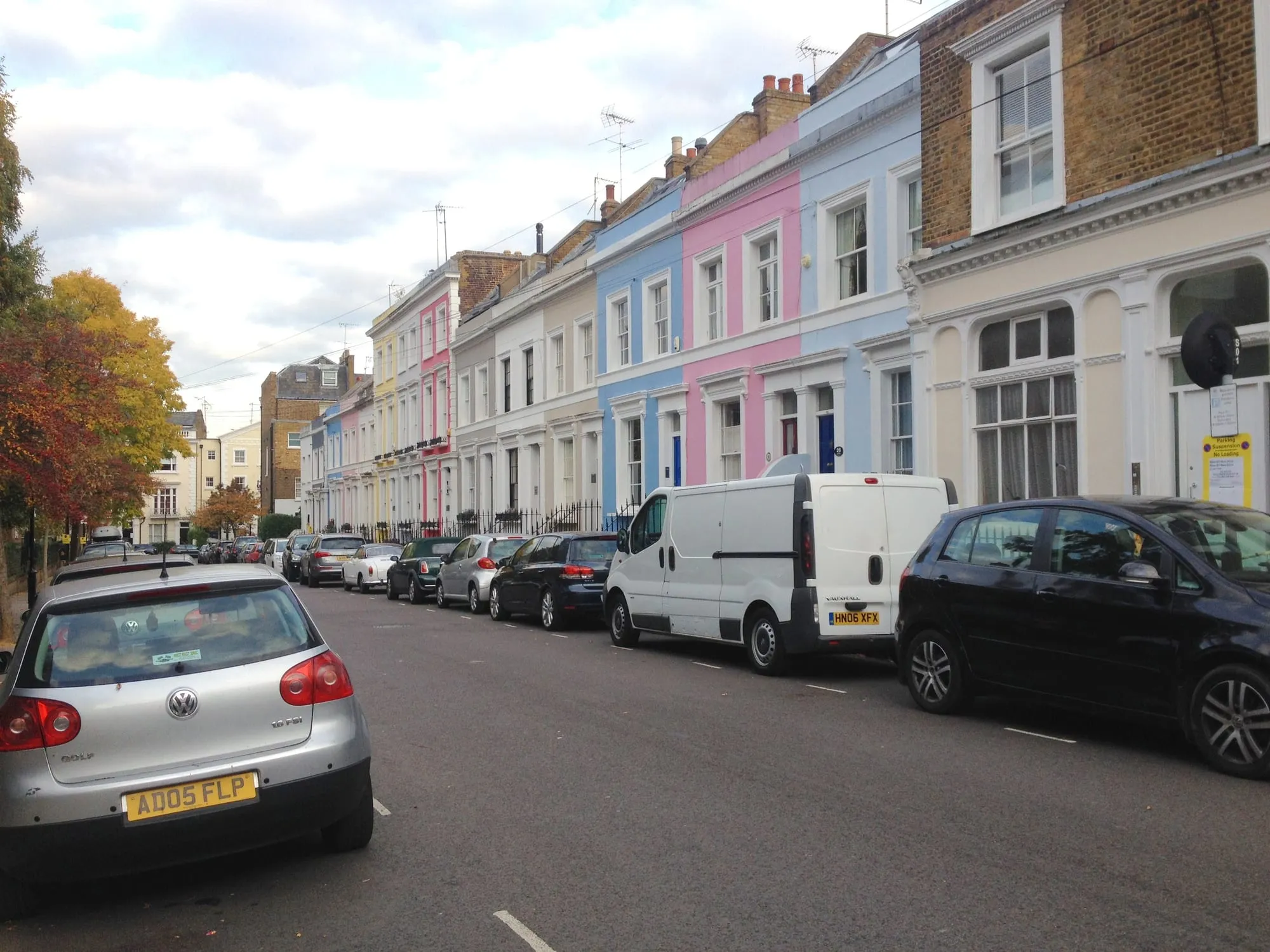 A terrace on Denbigh Terrace painted pink, blue, yellow and cream, seen along the parked cars