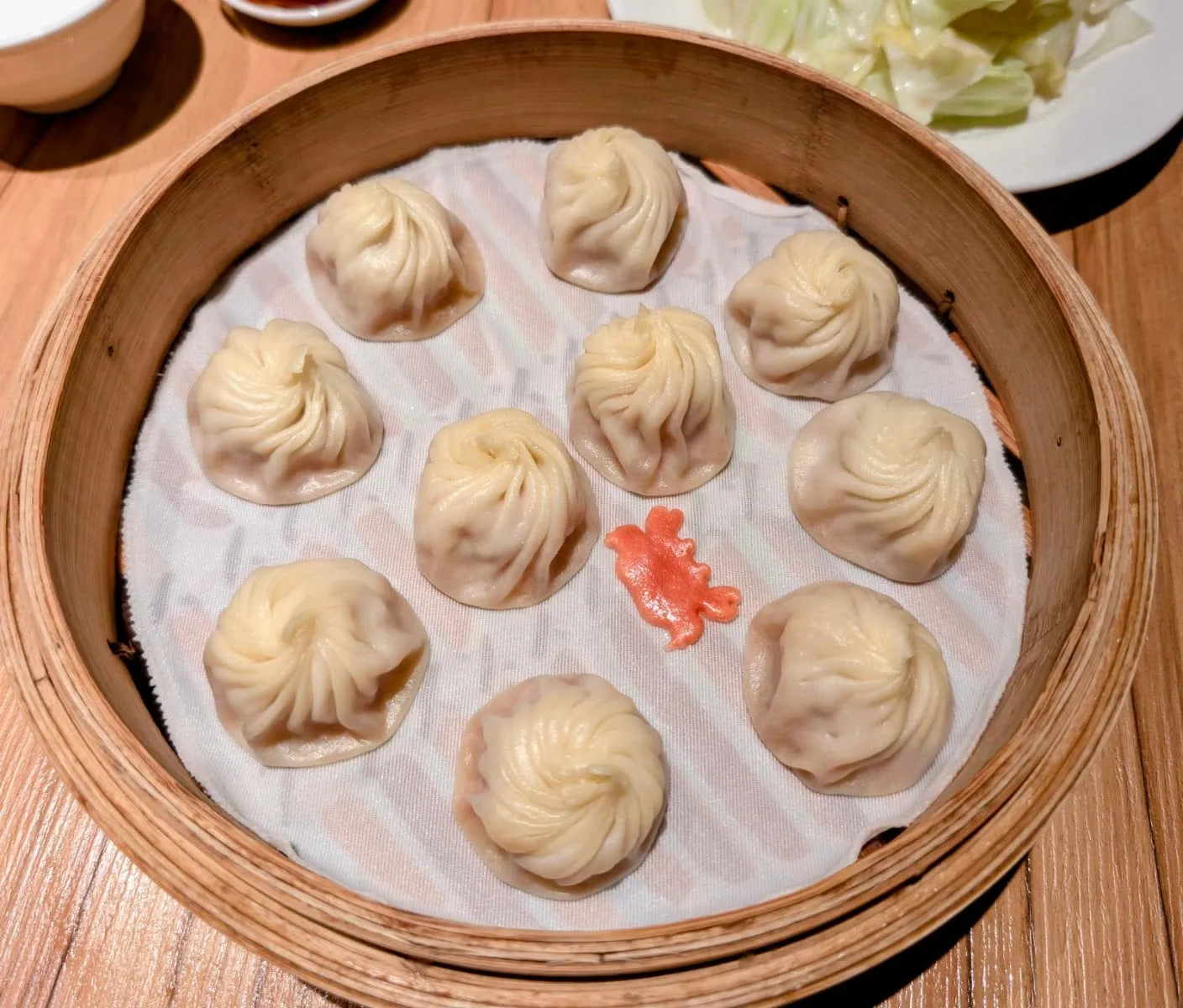 Ten xiao long bao arranged in a circle in a bamboo steamer, with a small red garnish in the centre