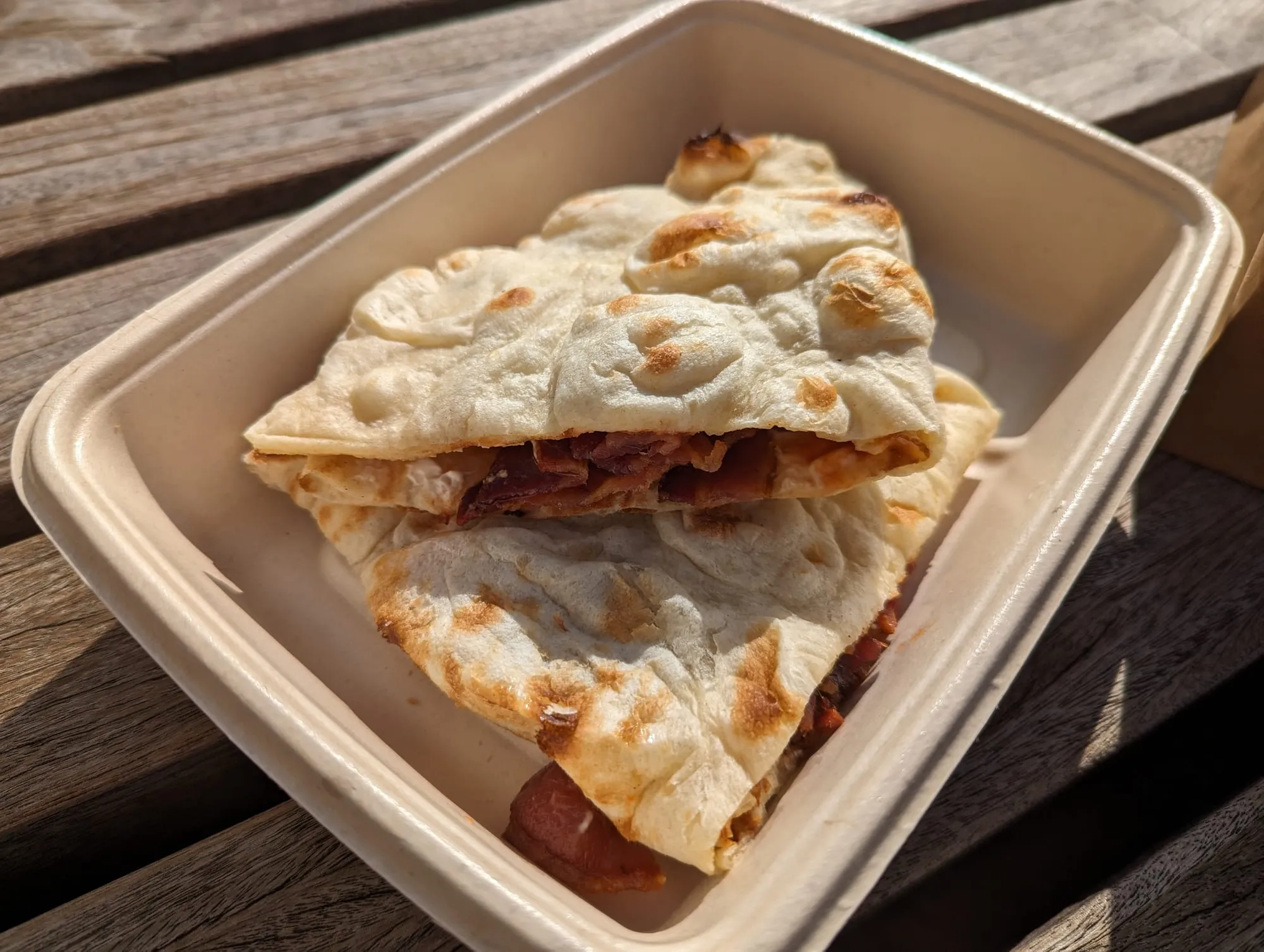 A bacon naan roll from Dishoom, folded open in a takeaway box