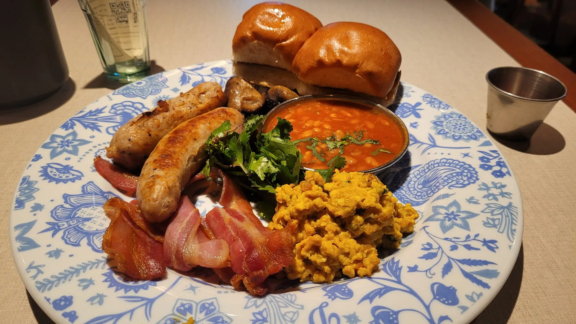 A Dishoom breakfast plate with bacon, sausages, mushrooms, baked beans, akuri scrambled eggs and buttered buns