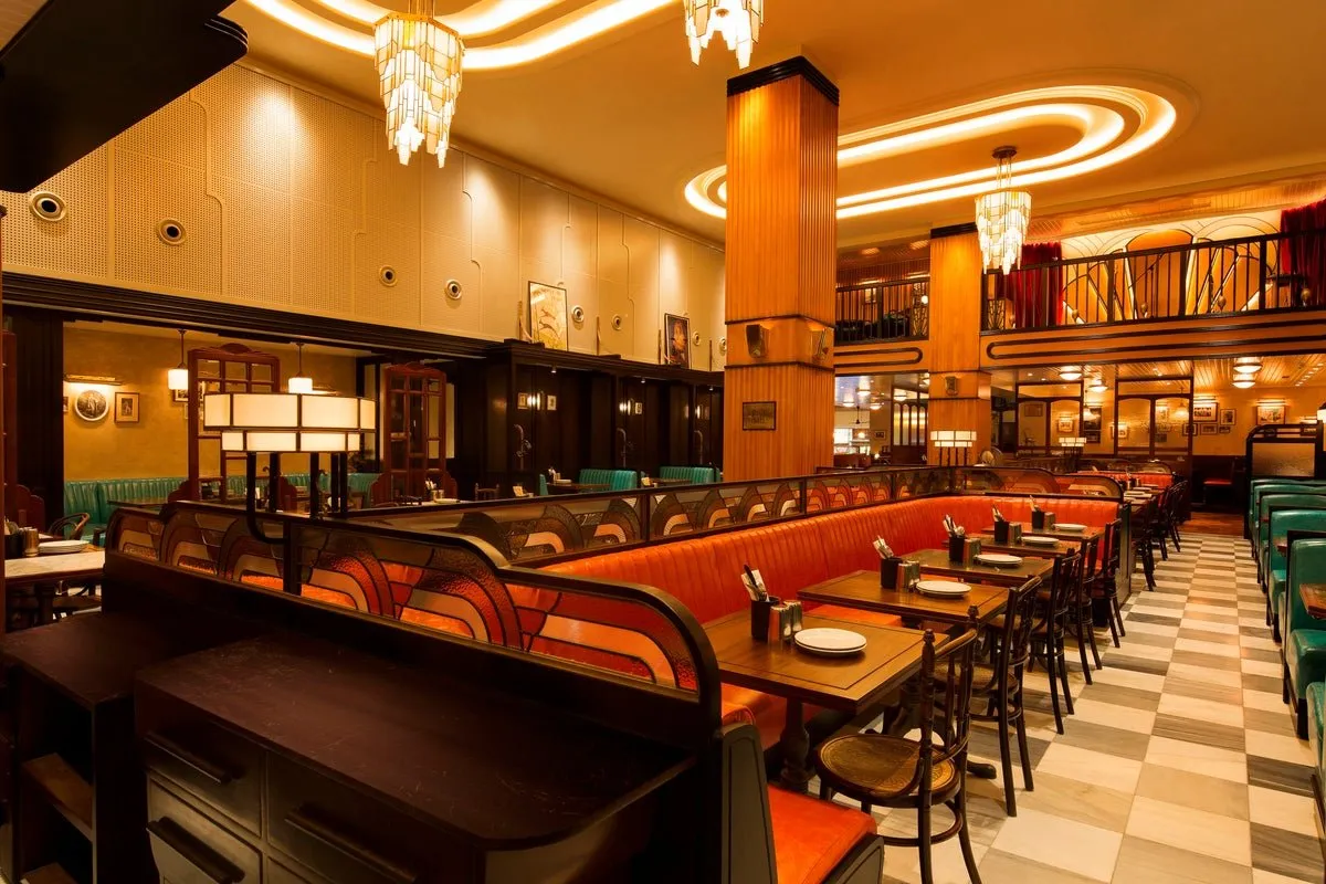 The Art Deco dining room at Dishoom Kensington, with orange leather booths, a chequerboard floor and a mezzanine gallery