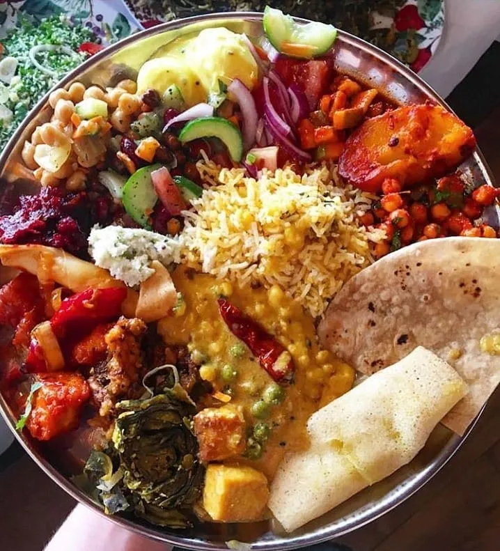 A loaded steel thali tray holding chana, dal with peas, a beetroot dish, salad, rice, chapati and a papad