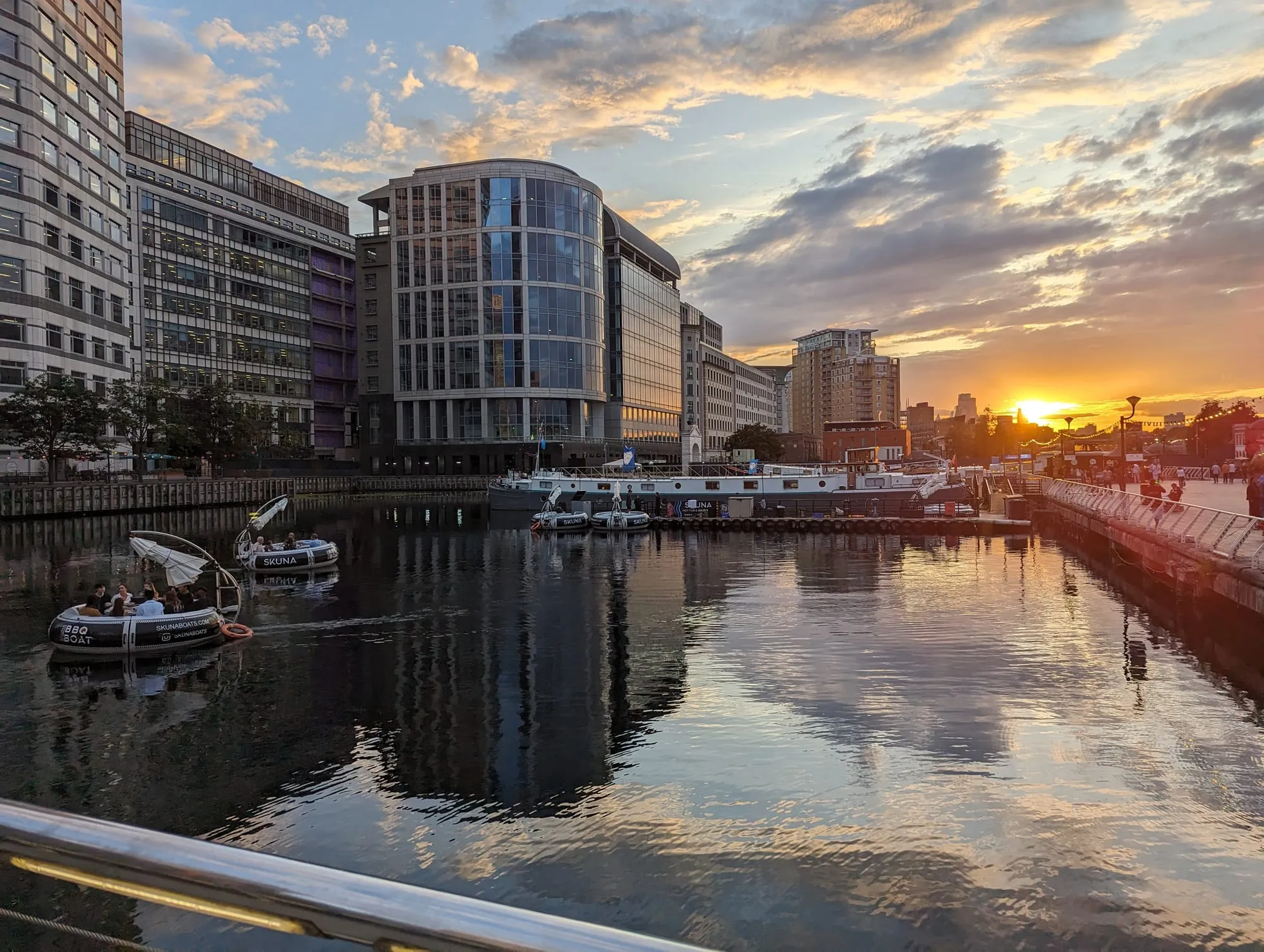 Office towers and moored boats reflected in a Canary Wharf dock at sunset