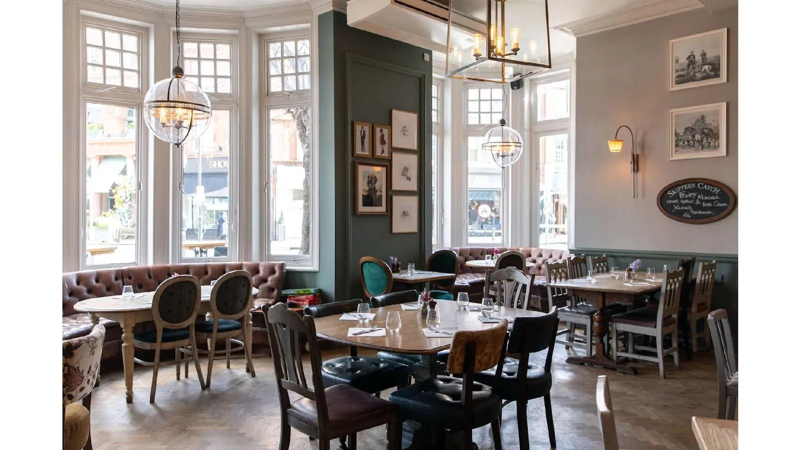 Inside the Dog & Fox: a bay-windowed dining room with leather banquettes, wooden tables and framed prints on a sage green wall