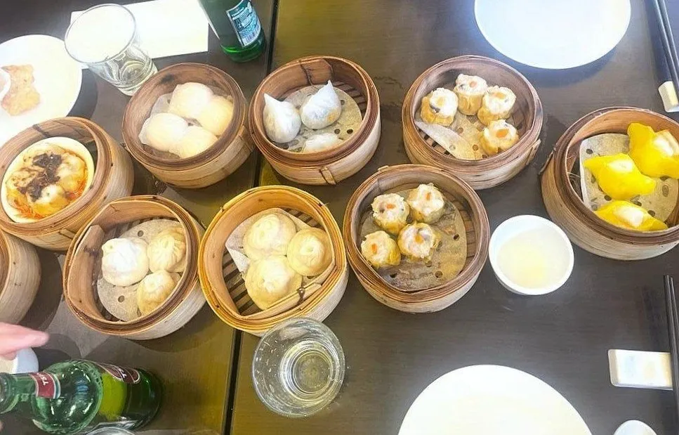 Eight bamboo steamers crowded onto a table, holding har gau, siu mai, char siu bao and yellow-wrapped dumplings