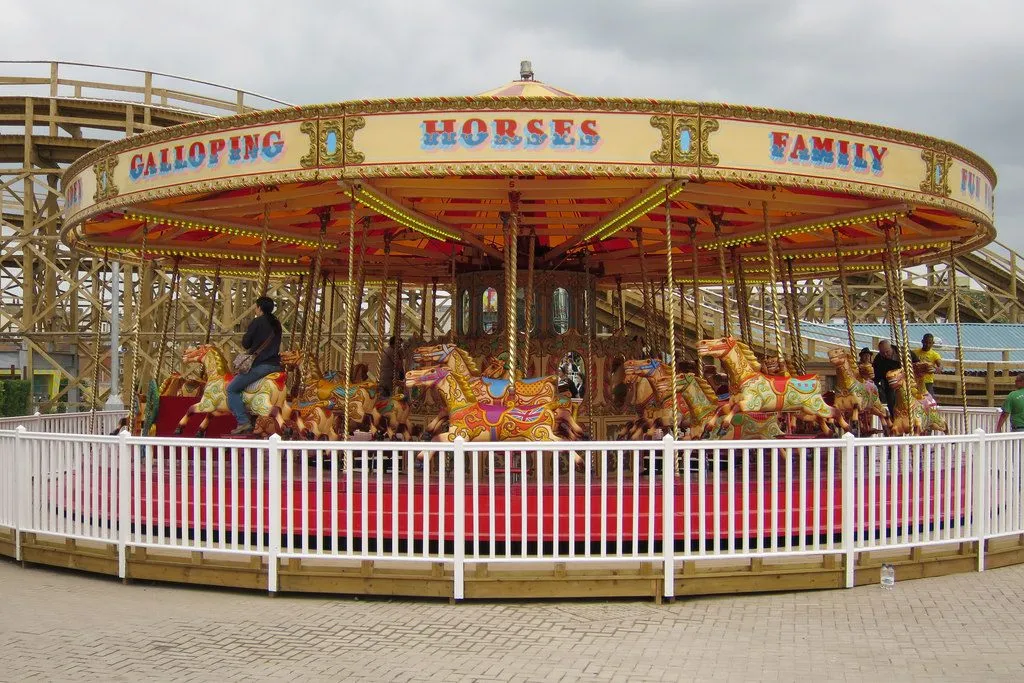The Galloping Horses carousel at Dreamland Margate, painted horses under a gold and red canopy, with the wooden Scenic Railway structure behind
