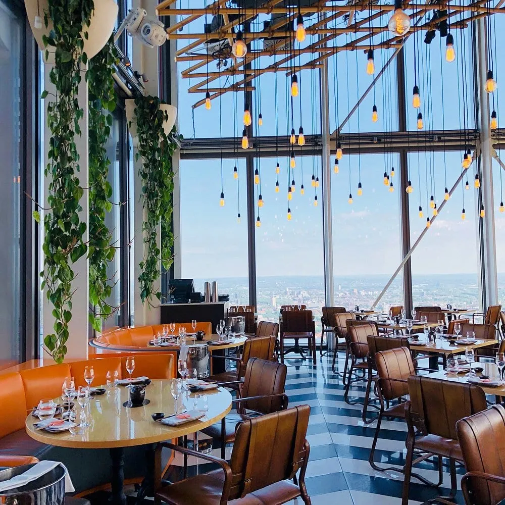 Duck & Waffle's dining room on the fortieth floor, floor-to-ceiling windows over London with hanging bulbs and trailing plants