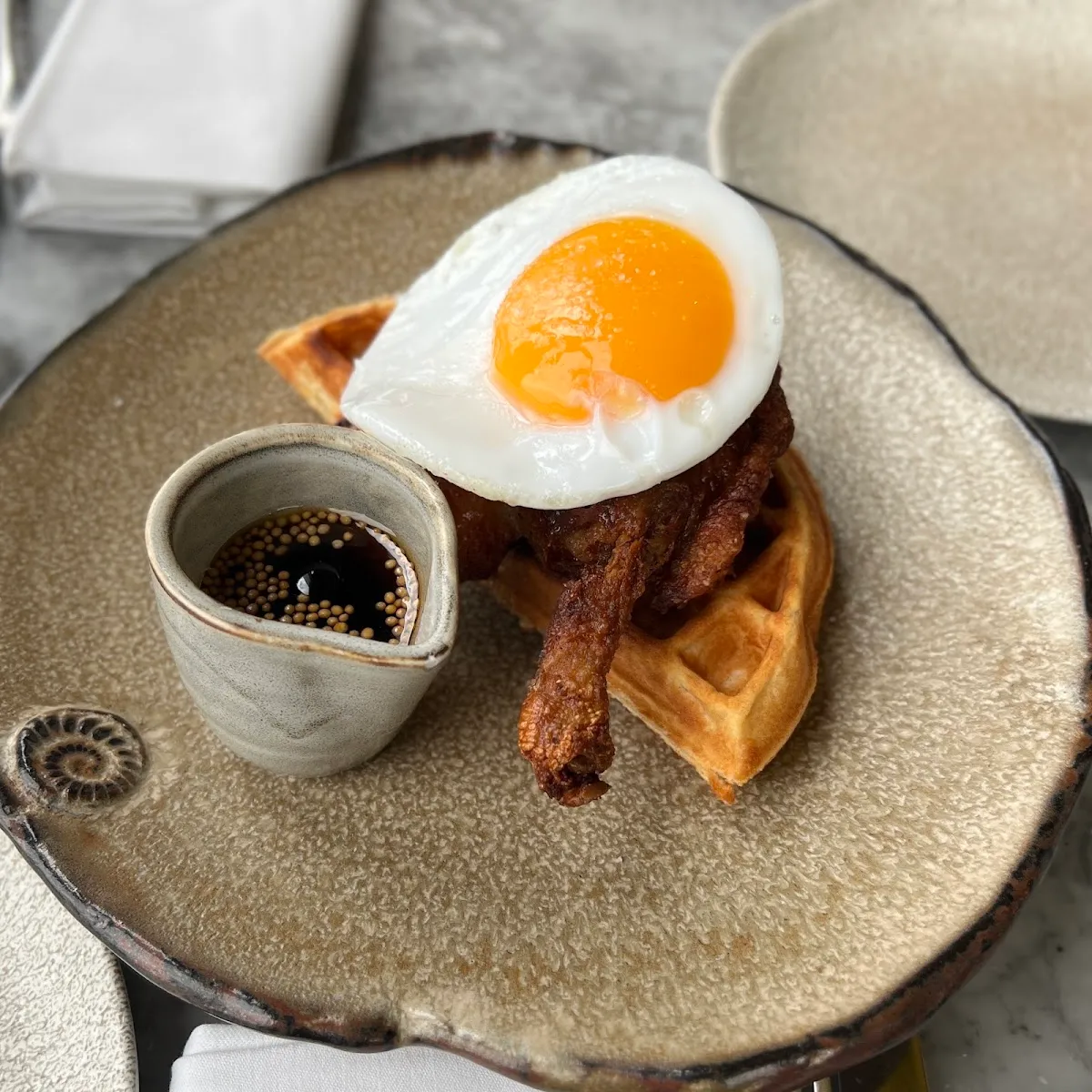 The Duck & Waffle signature dish: confit duck leg and a fried egg on a waffle, with a small pot of mustard maple syrup