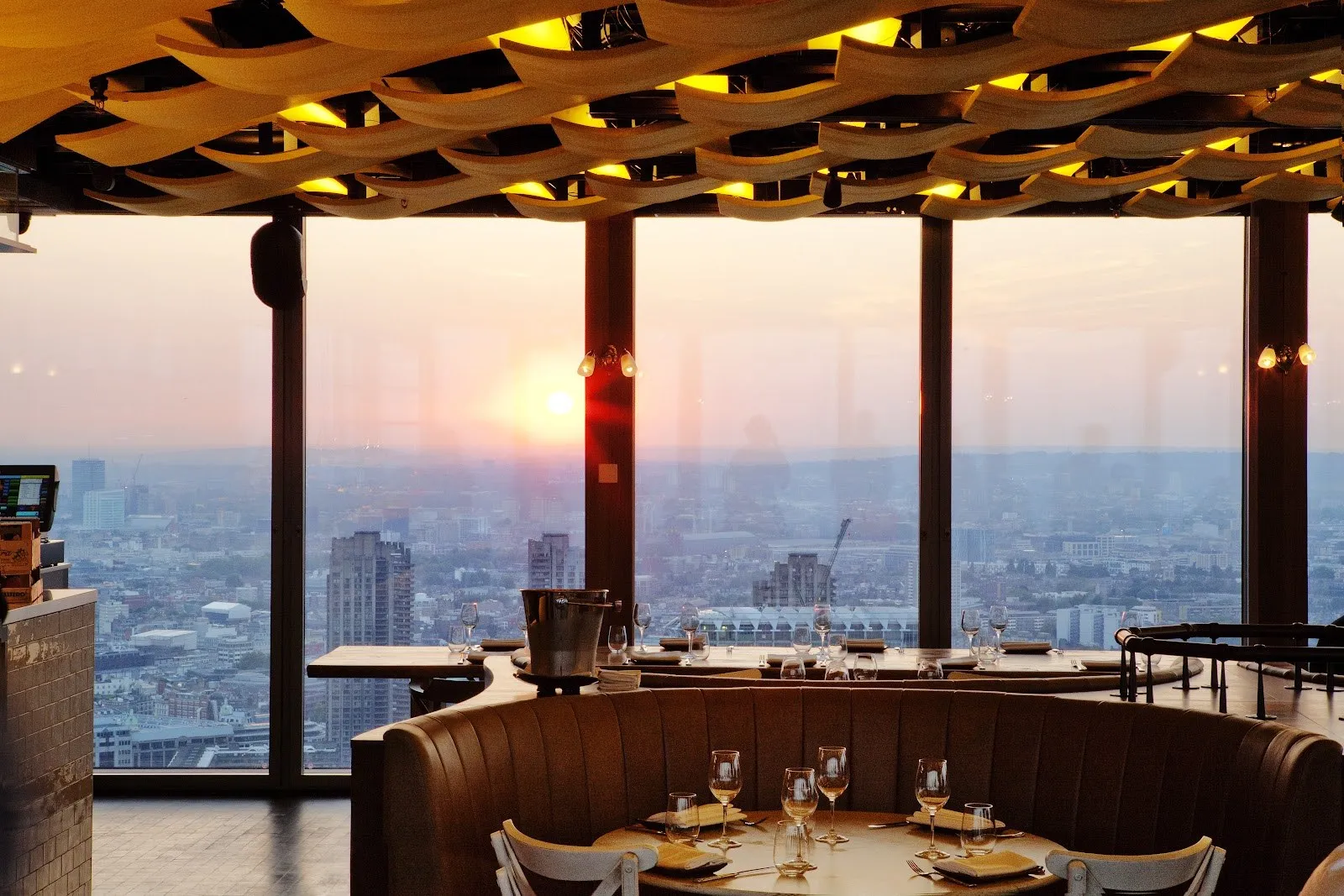 A curved booth and tables by floor-to-ceiling windows at sunset