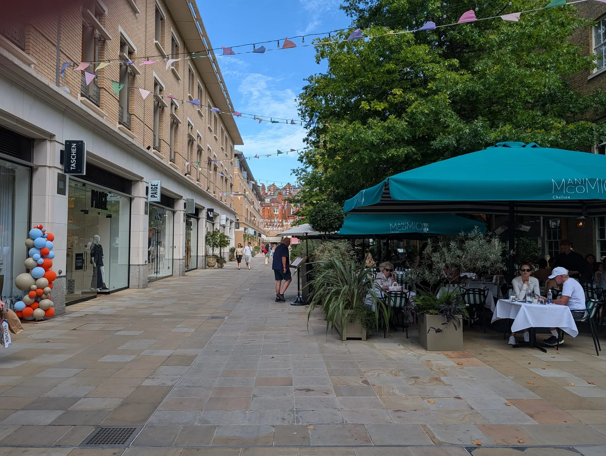 Shops and outdoor dining along Duke of York Square, with bunting overhead