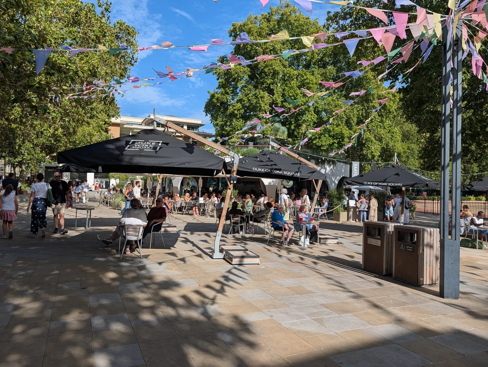 Outdoor tables under umbrellas and bunting at Duke of York Square off the King's Road