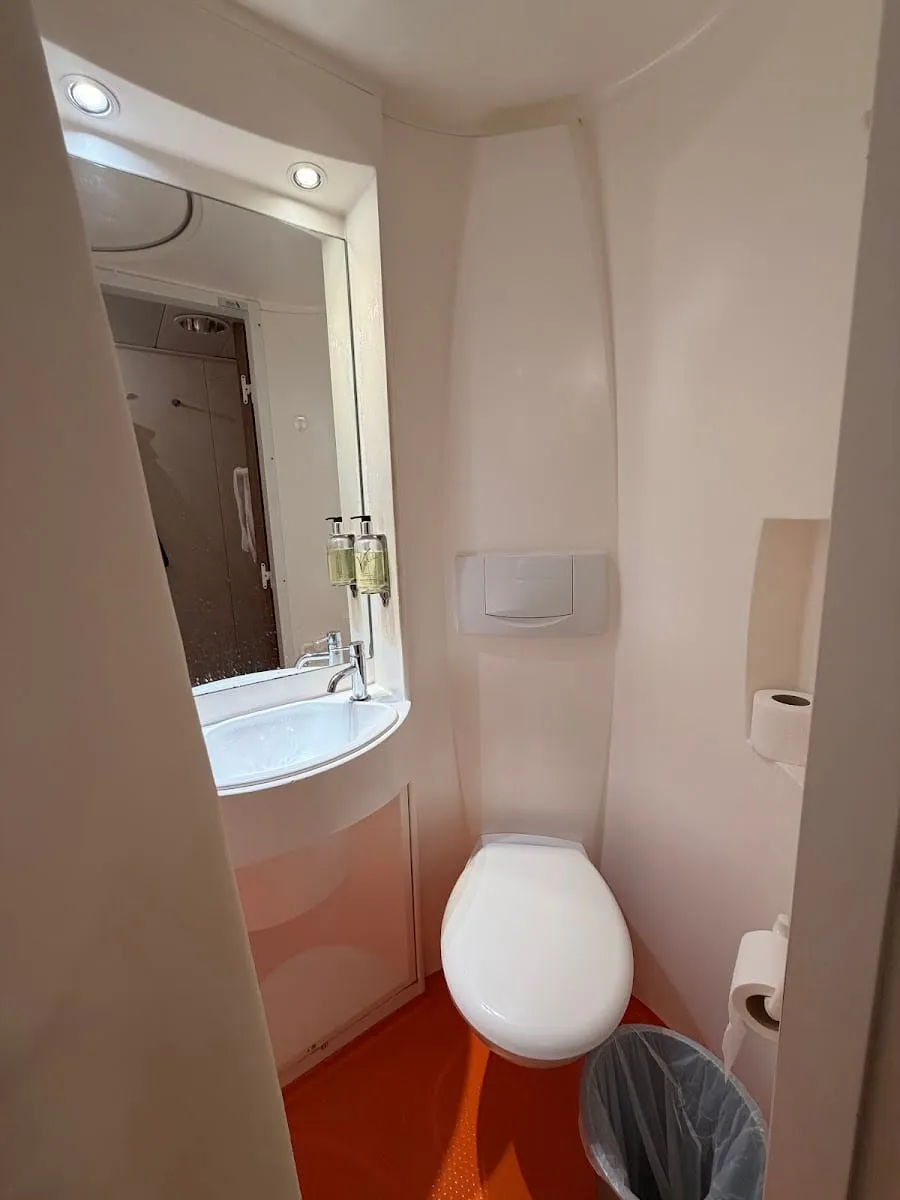 The ensuite bathroom of an easyHotel South Kensington room, with an orange floor and a curved moulded unit holding the toilet and basin