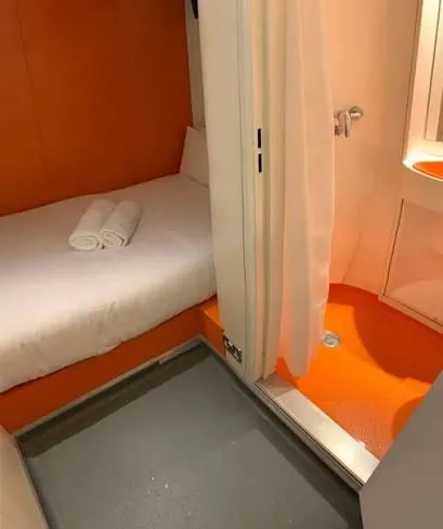 A windowless room at easyHotel South Kensington, with an orange accent wall and the ensuite shower visible through the open door