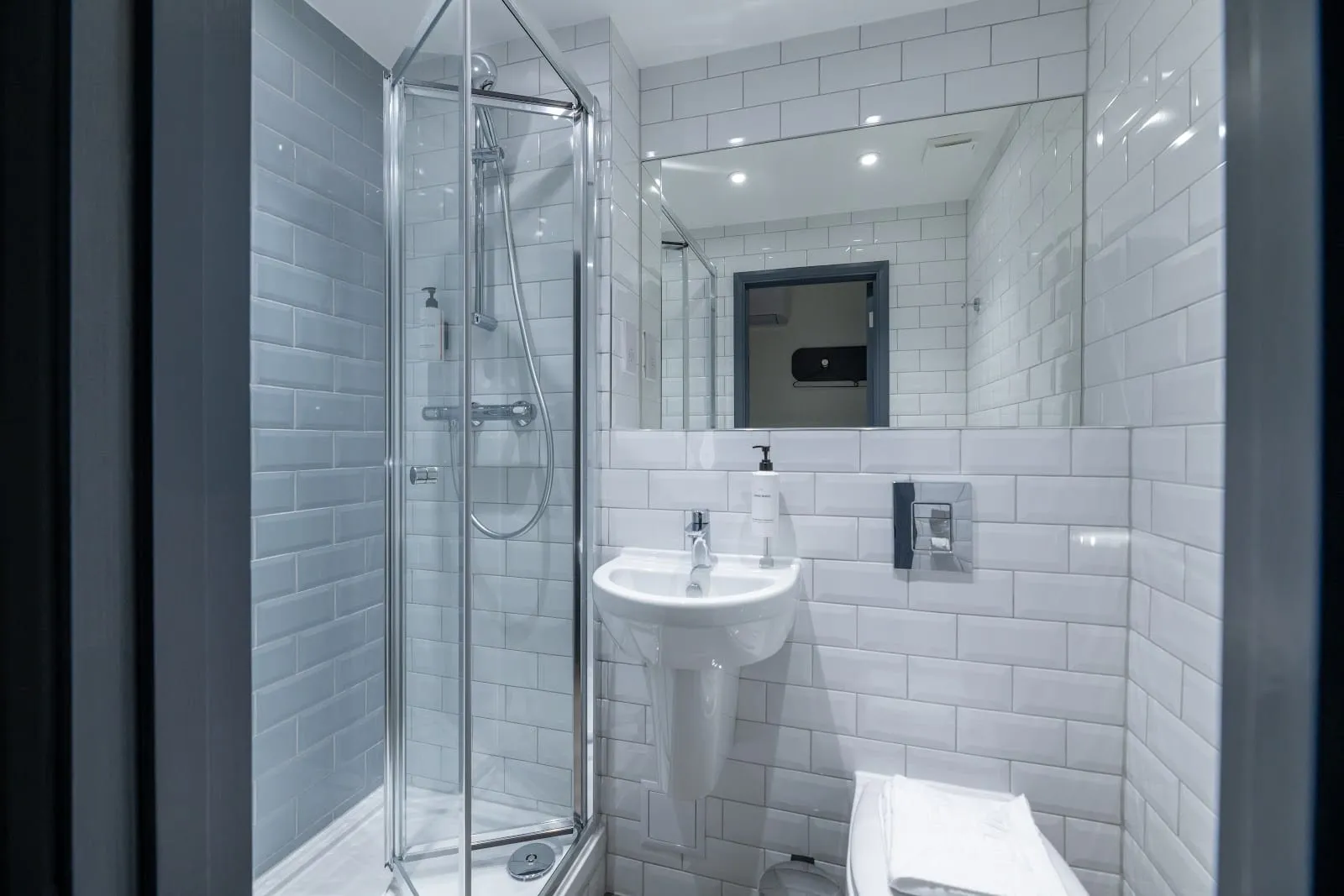 The ensuite bathroom of an easyHotel Victoria room, with white subway tile and a glass shower cubicle