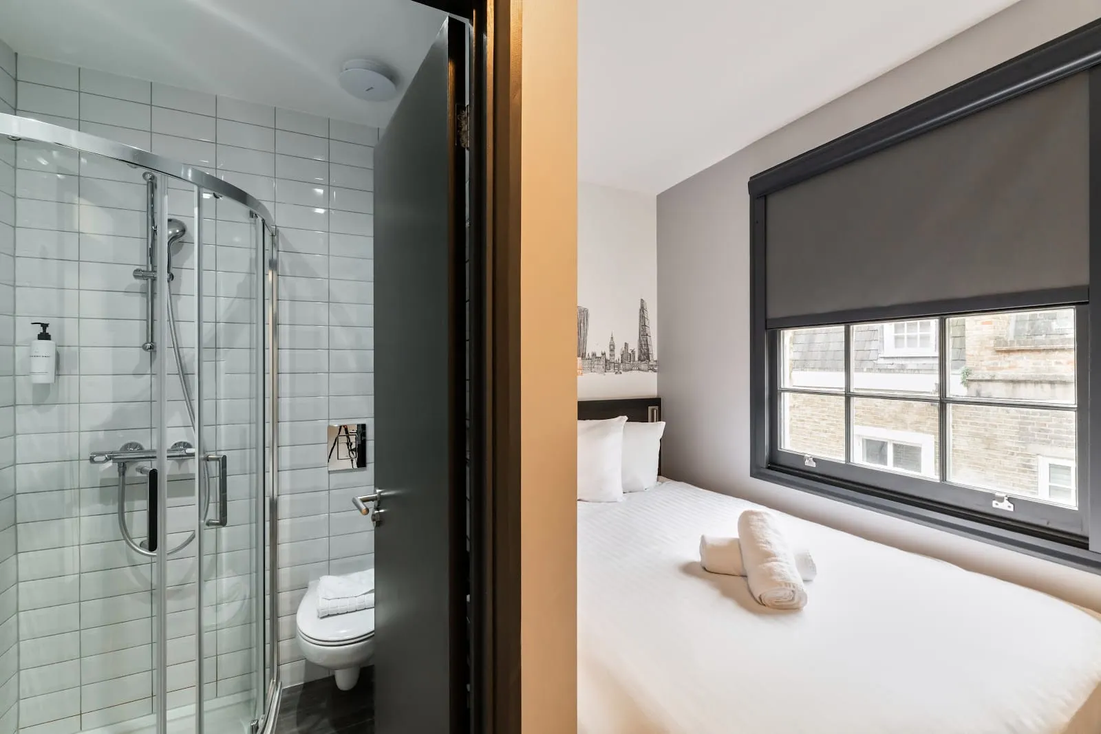 A room at easyHotel Victoria with a London skyline mural above the headboard and a window looking onto the building opposite