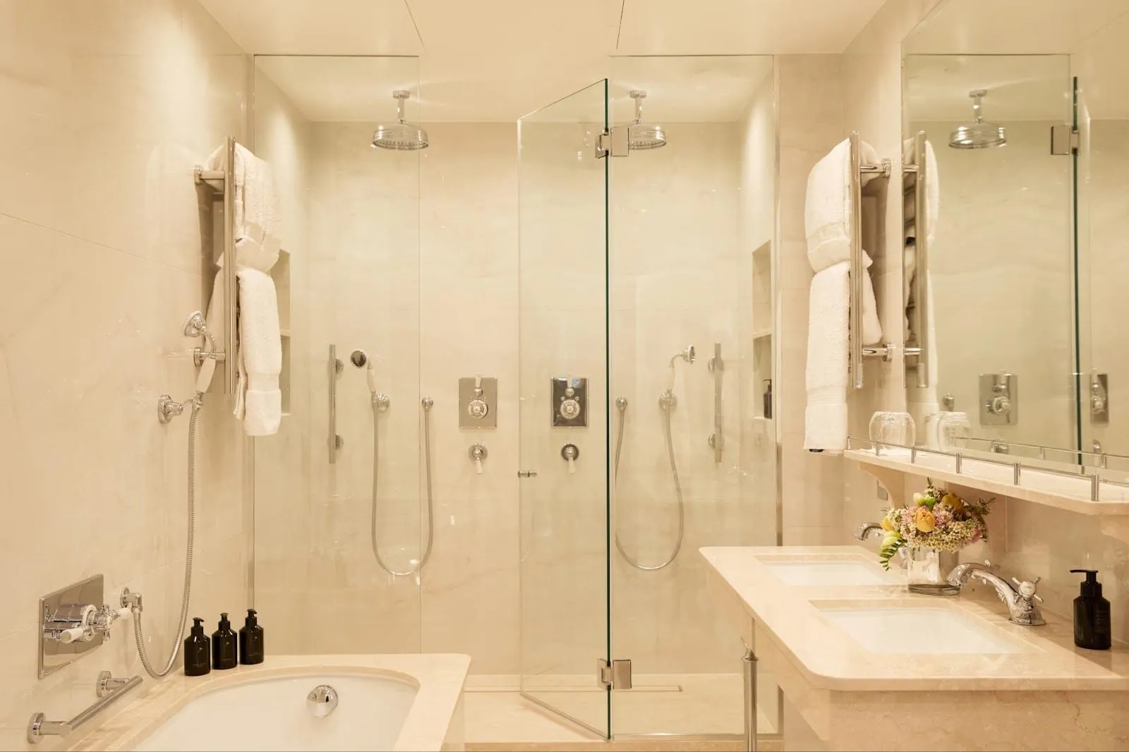 The marble bathroom of the V&A Suite at Egerton House, with a bath, a walk-in shower for two behind glass with twin rainfall heads, and twin basins
