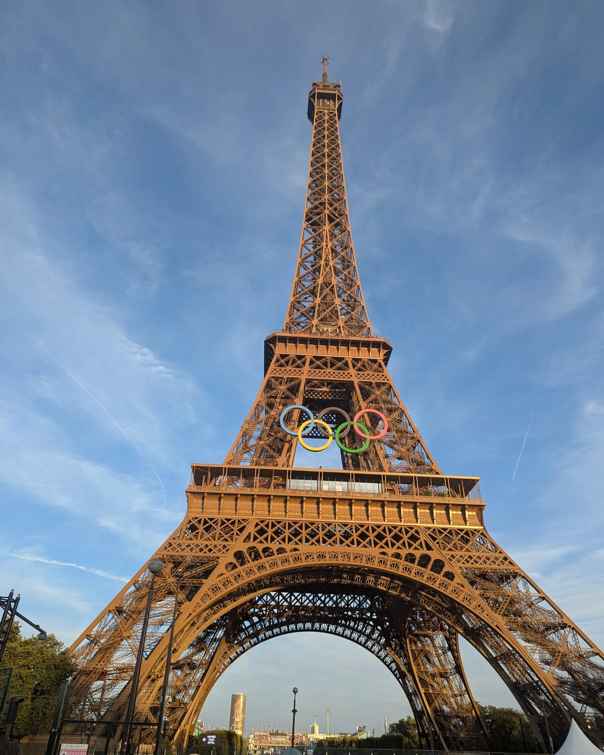The Eiffel Tower seen from below on a sunny evening, with the five Olympic rings mounted between the first and second floors
