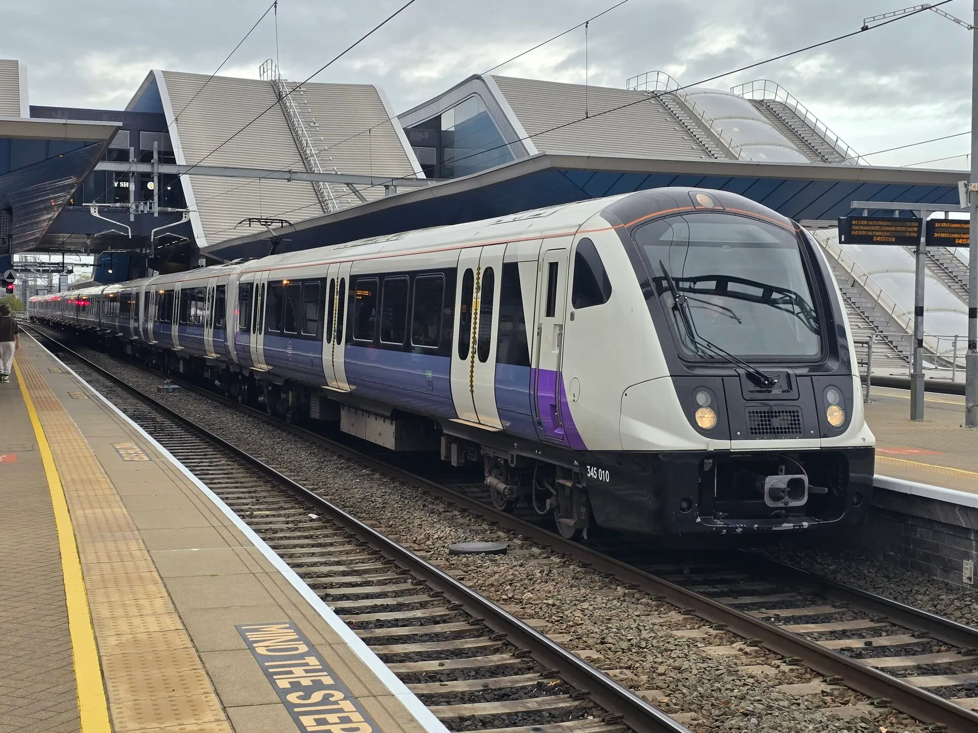 A purple and white Elizabeth line train standing at Reading station