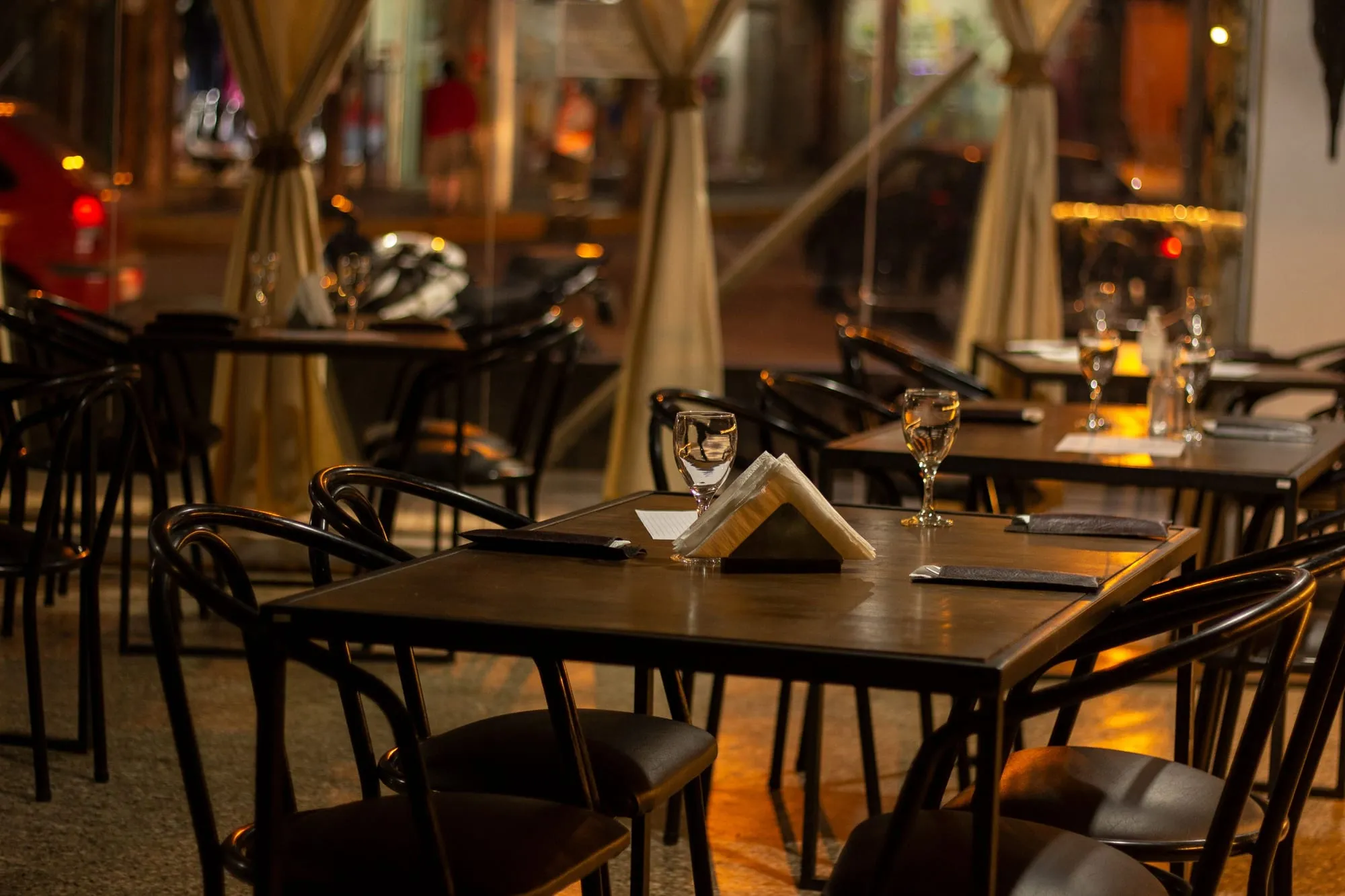 An empty restaurant dining room in the evening, tables laid with wine glasses and napkins under warm lighting, every chair unoccupied