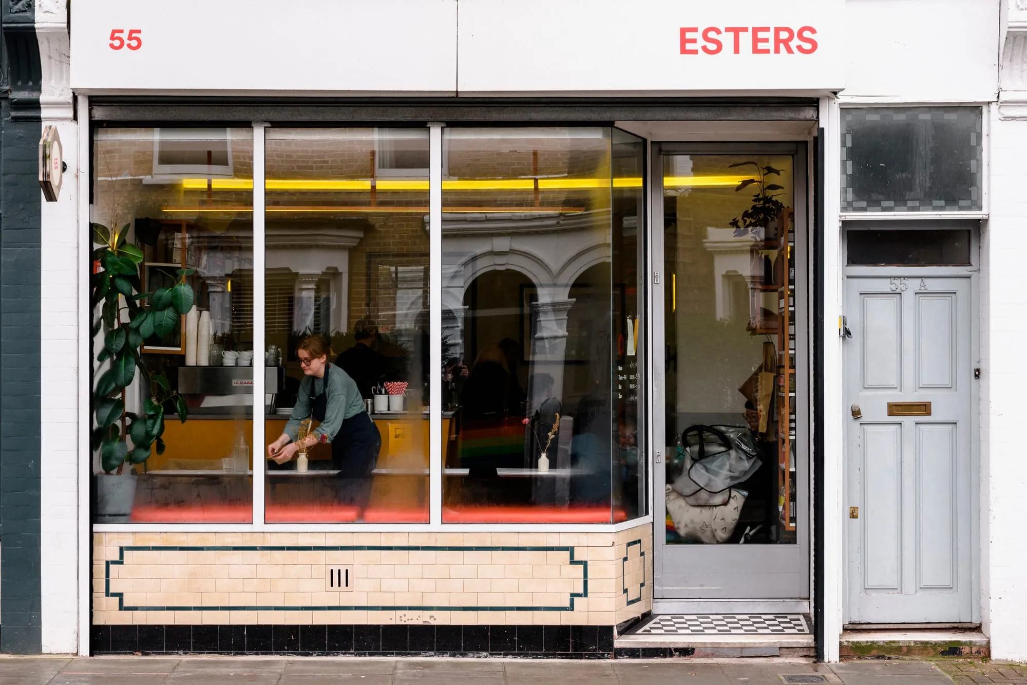 The shopfront of Esters at 55 Stoke Newington Church Street, a member of staff laying a table inside the window