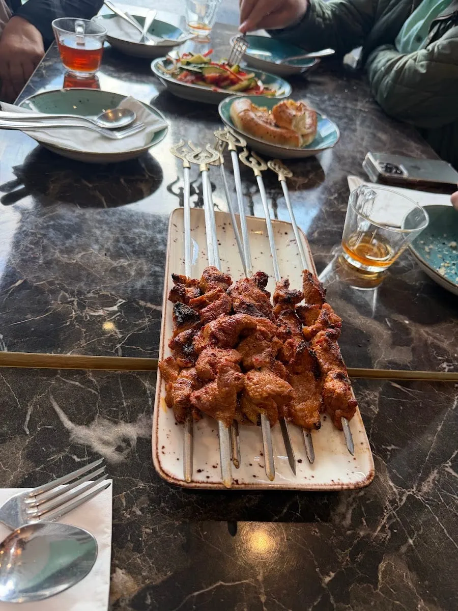 Six lamb skewers, grilled and charred, arranged on a rectangular plate with metal skewer handles