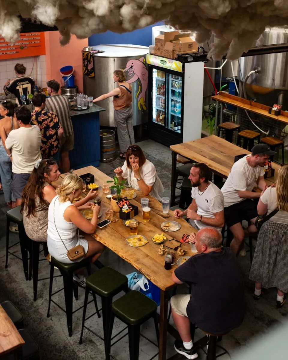 An elevated view of Exale's taproom, with a steel fermentation tank beside communal wooden tables where people are eating and drinking