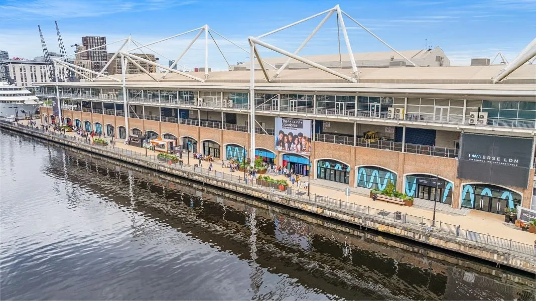 ExCeL London's brick waterfront frontage and glass canopy along Royal Victoria Dock, with the Immerse LDN sign visible on the building