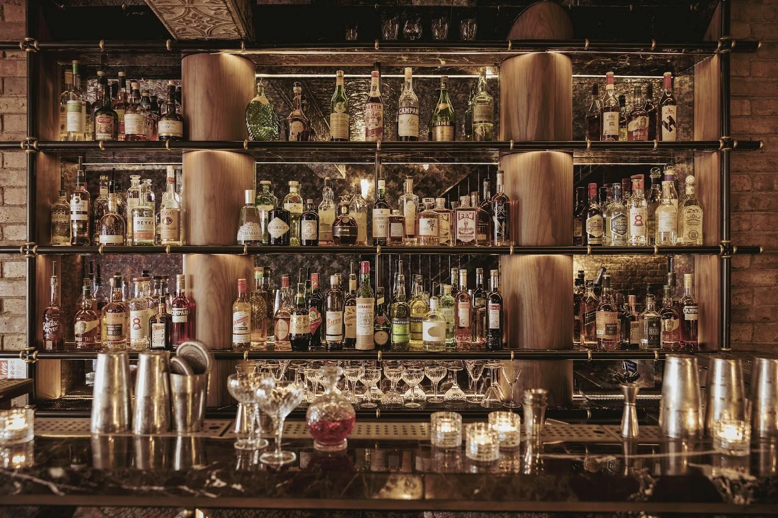 The back bar at Experimental Cocktail Club, shelves of bottles between curved wooden columns, with shakers and glasses on a marble counter
