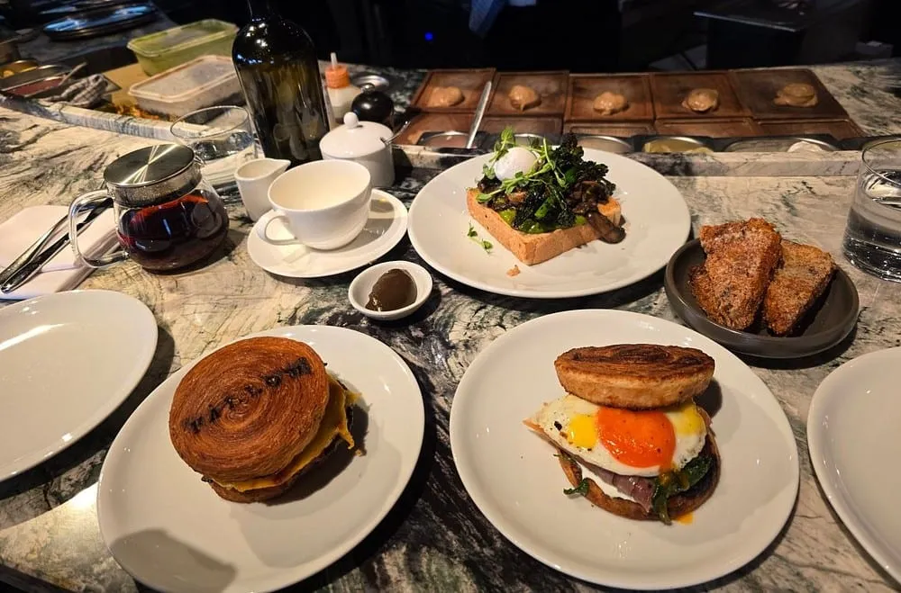 Brunch at Fallow on a marble counter: a croissant sandwich, an egg-topped muffin and mushrooms on toast