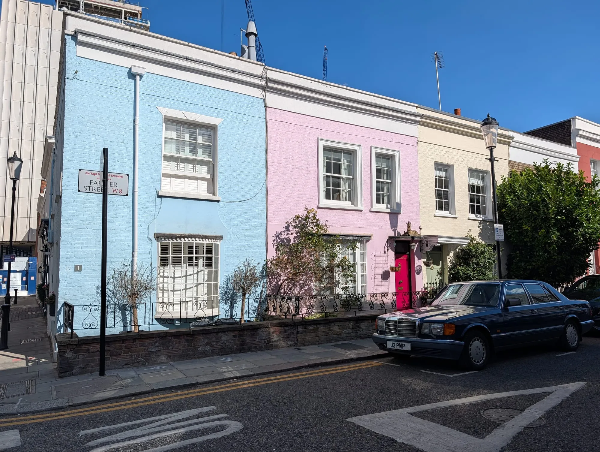 A terrace of small houses on Farmer Street painted blue, pink and cream, with a classic car parked outside