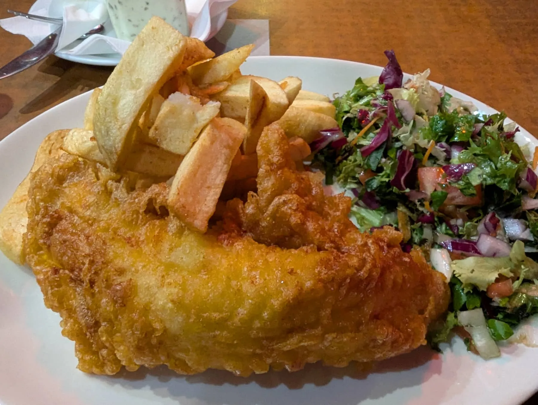 A plate of battered fish with thick hand-cut chips and a side salad at a Greenwich chip shop