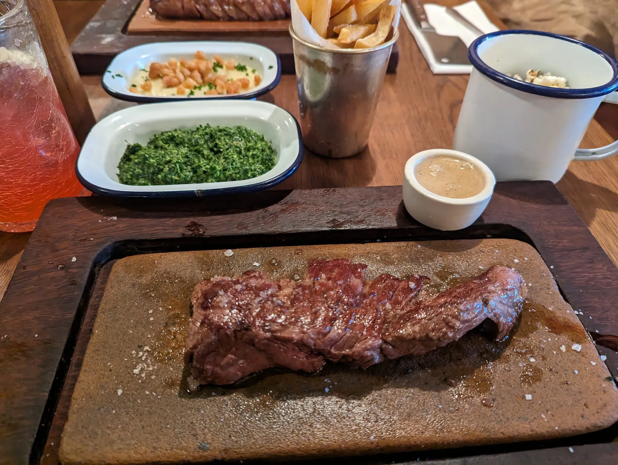 A flat iron steak sliced on a wooden board with creamed spinach and beef dripping chips