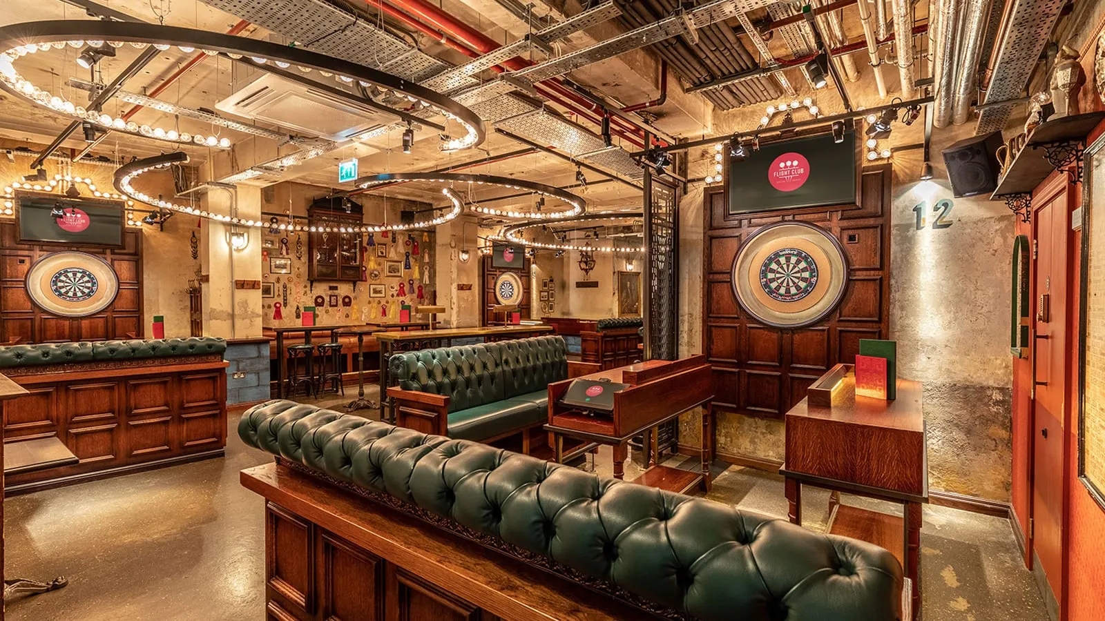 A darts bay at Flight Club, with a board set in oak panelling, deep green leather booths and rings of bare bulbs hung from an exposed-pipe ceiling