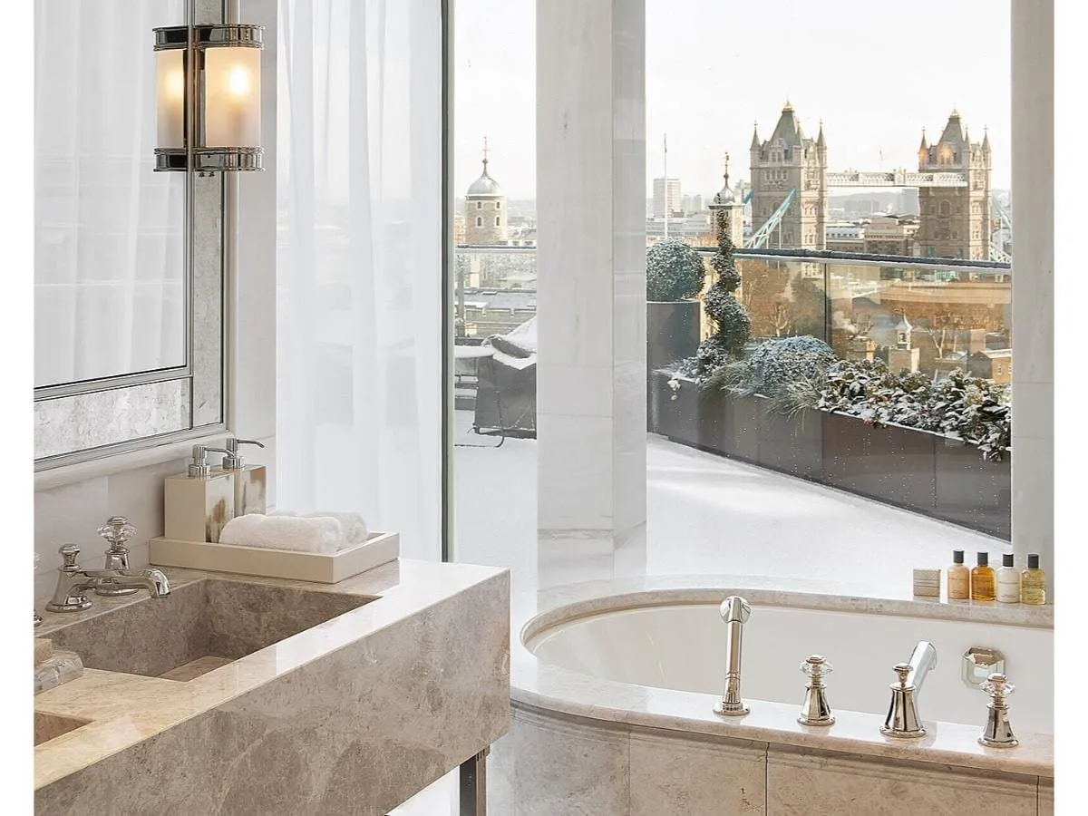 A marble bathroom at the Four Seasons at Tower Bridge with a bath set in marble and nickel taps, beside a window onto a snow-covered terrace looking at Tower Bridge and the White Tower