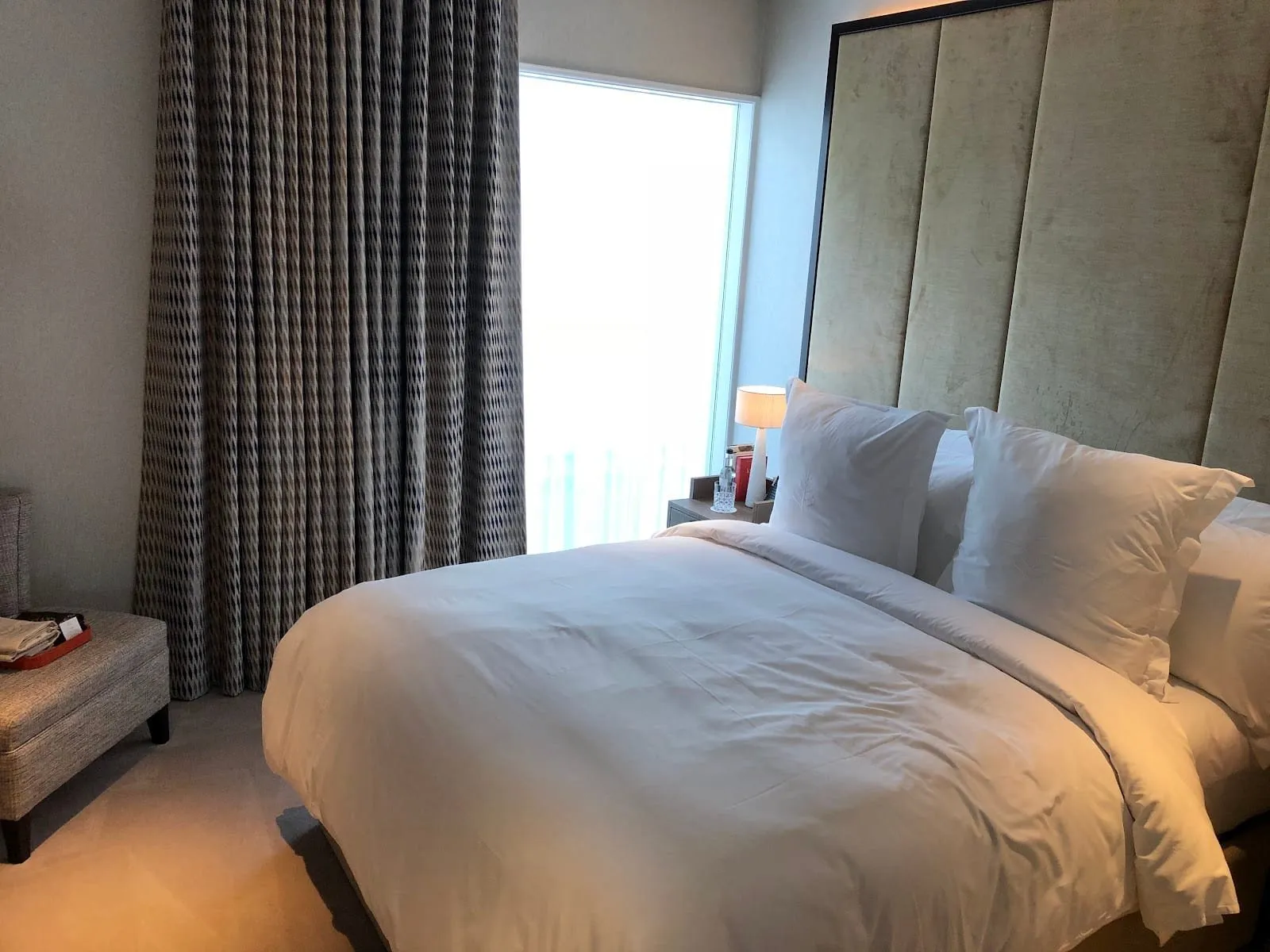A room at the Four Seasons at Tower Bridge: a double bed with Four Seasons pillows against a gold velvet headboard panelled almost to the ceiling, patterned curtains and a tall window