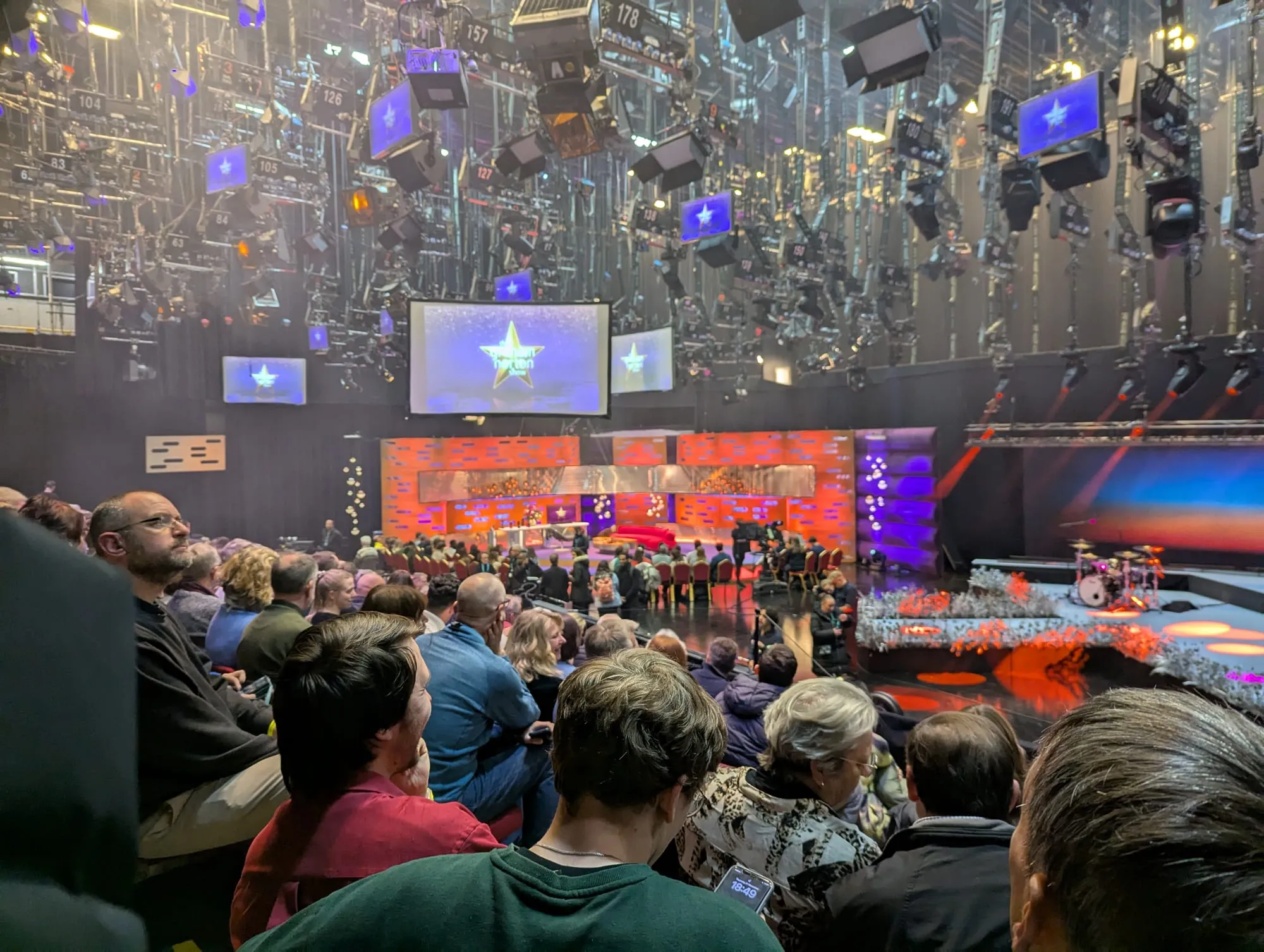 The Graham Norton Show studio seen from an audience seat, the lighting rig hung with hundreds of numbered lamps above the orange set and the red sofa