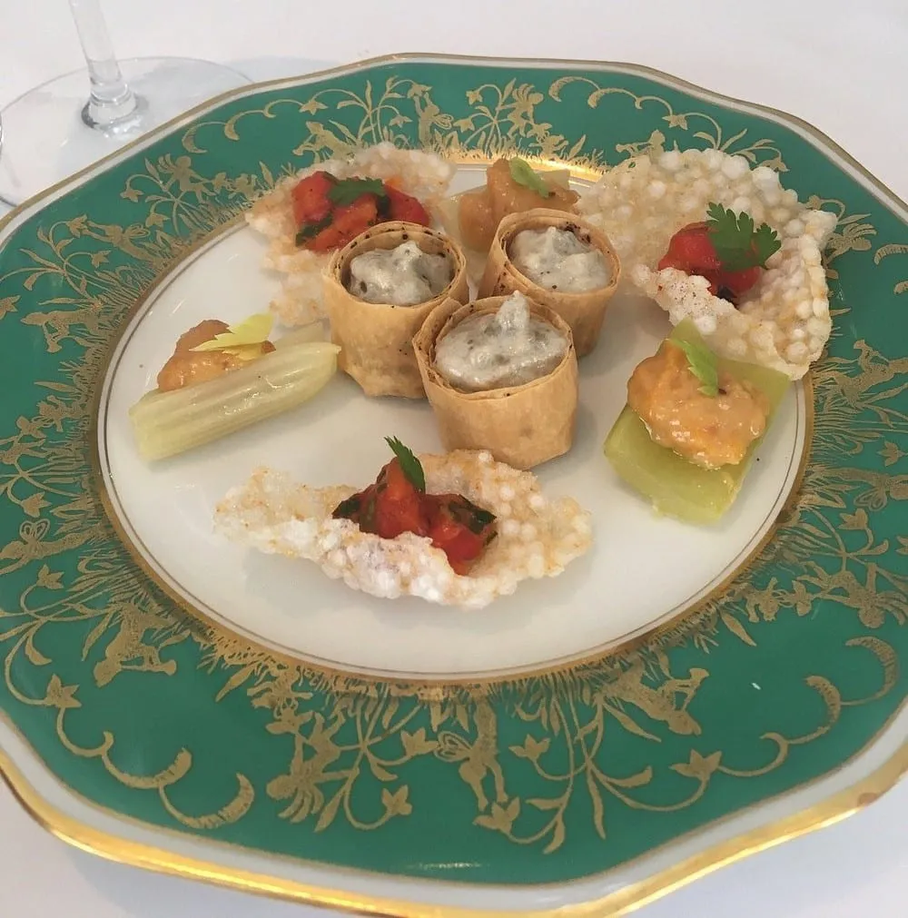 Canapés arranged on ornate green and gold china: filled tuile rolls, crisp rice crackers topped with tomato, and celery with an orange purée