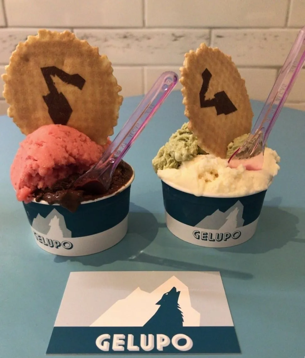 Two Gelupo tubs on a blue counter, each topped with a wafer stamped with the shop's wolf logo, beside a Gelupo card