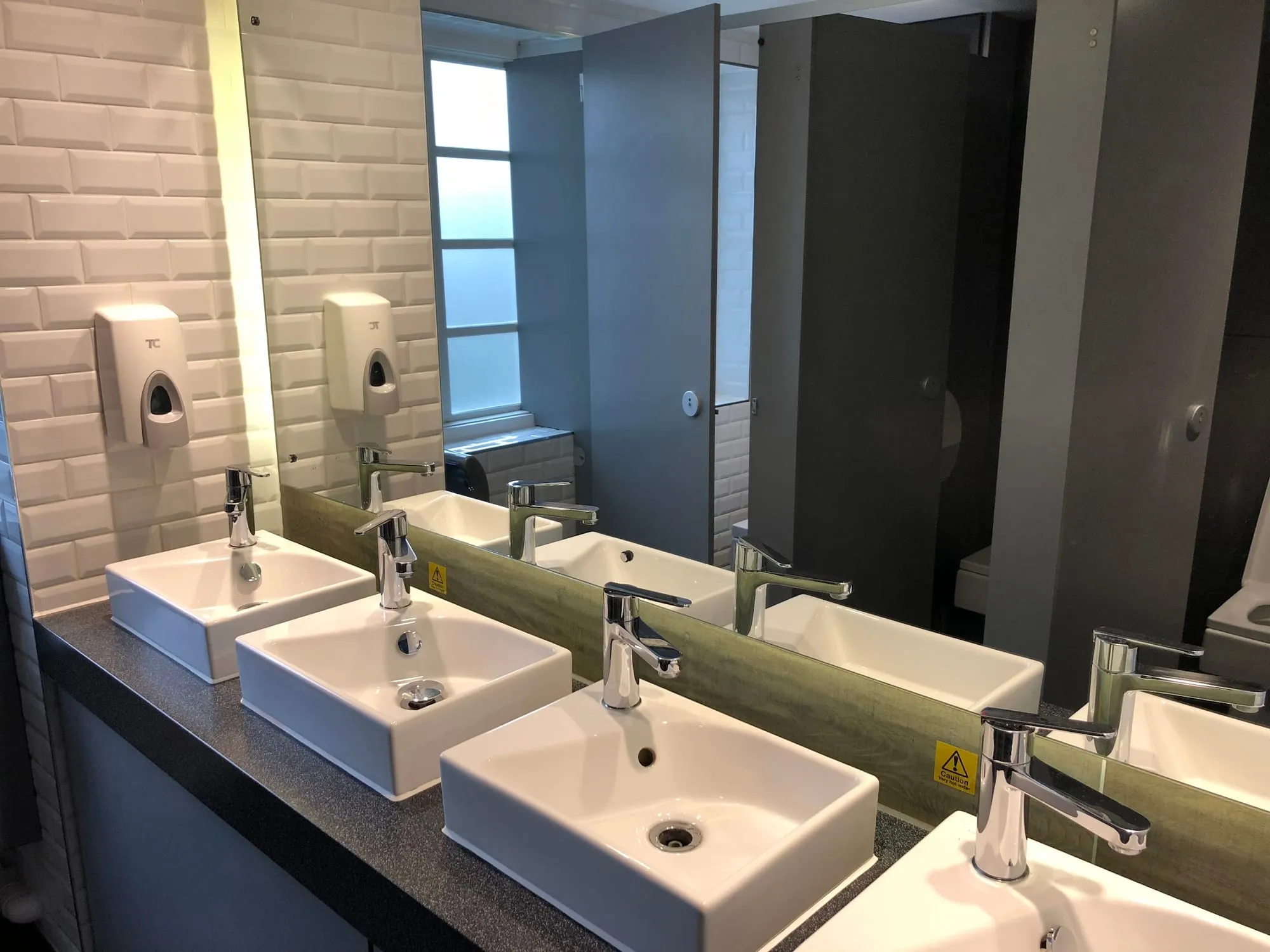 The shared bathroom at Generator London, with white subway tile, wall-mounted soap dispensers and a row of sink basins below a long mirror