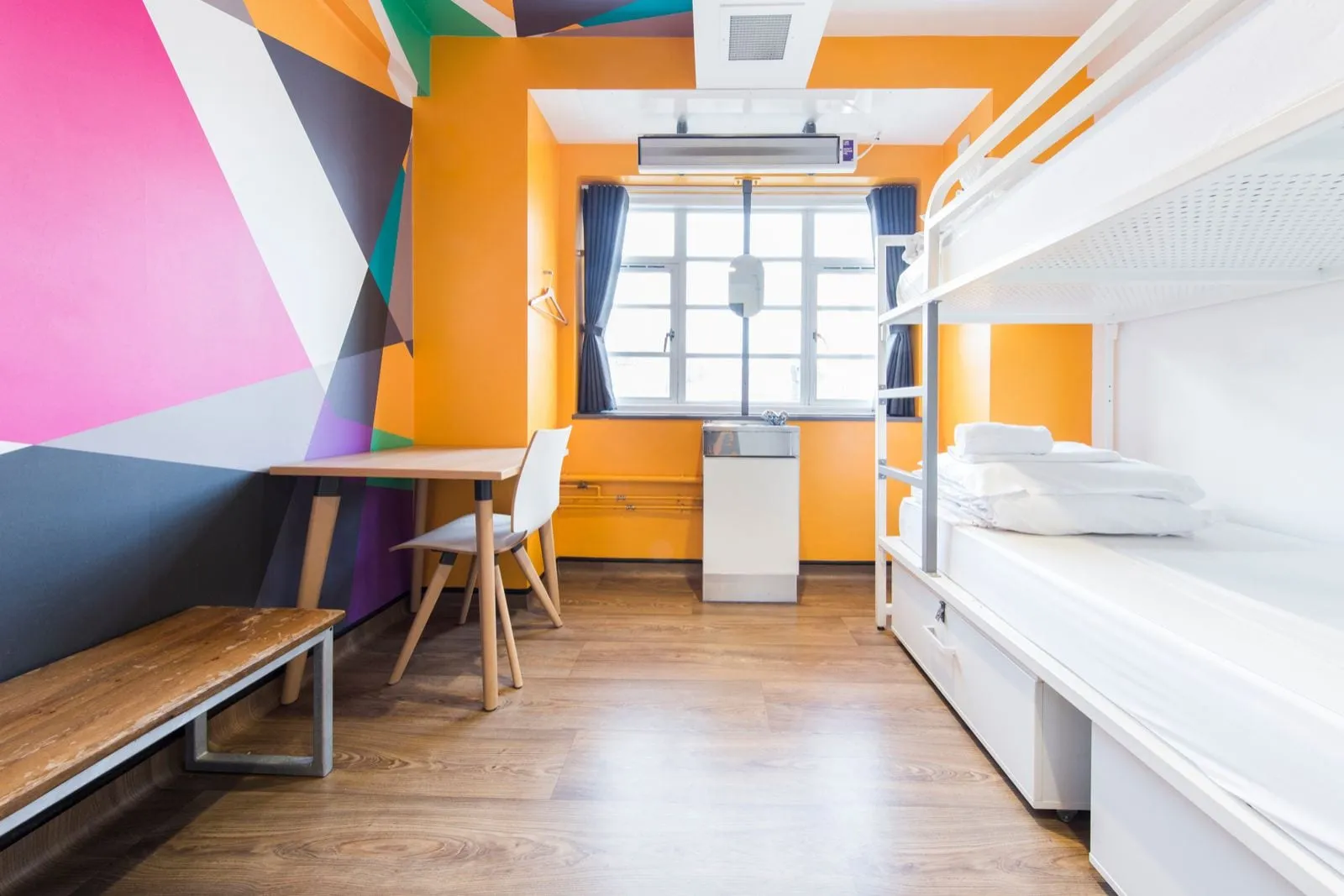 A Generator London dorm room with a bright pink, orange and teal geometric wall mural, bunk beds and a small desk