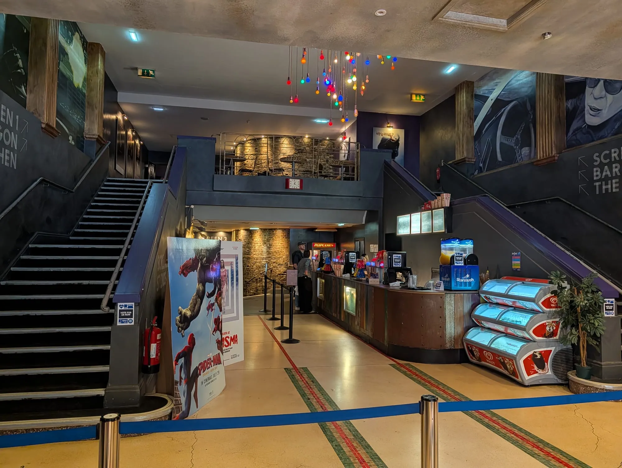 The foyer of the Genesis Cinema, with the box office counter, a staircase to the bar and strings of coloured lights overhead