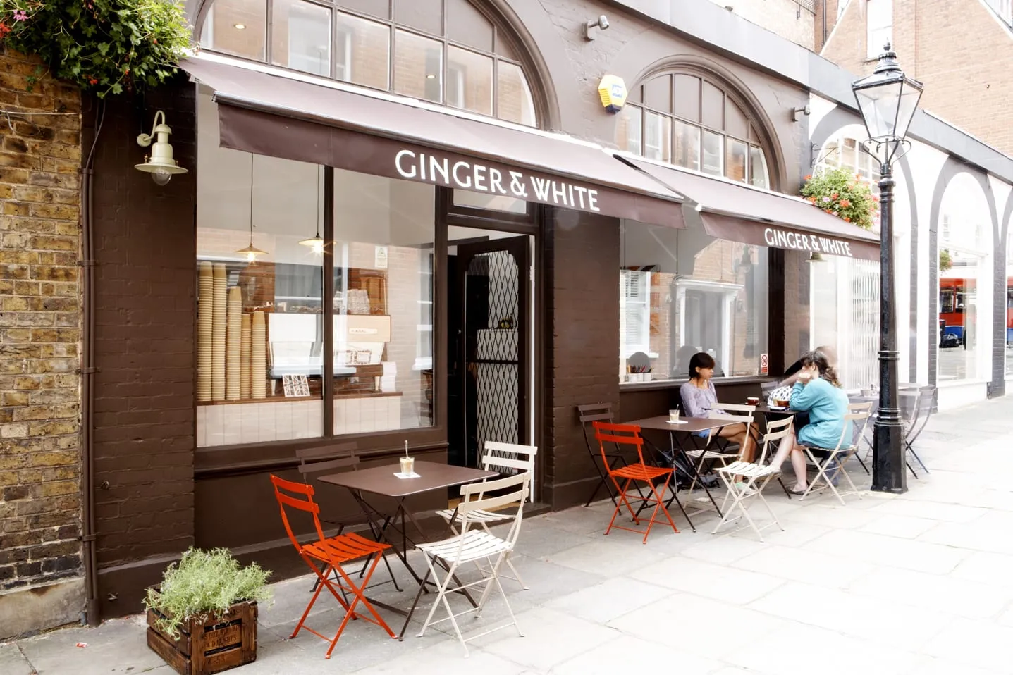 Ginger & White's brown shopfront on Perrins Court, with red and cream outdoor tables and chairs on the pavement