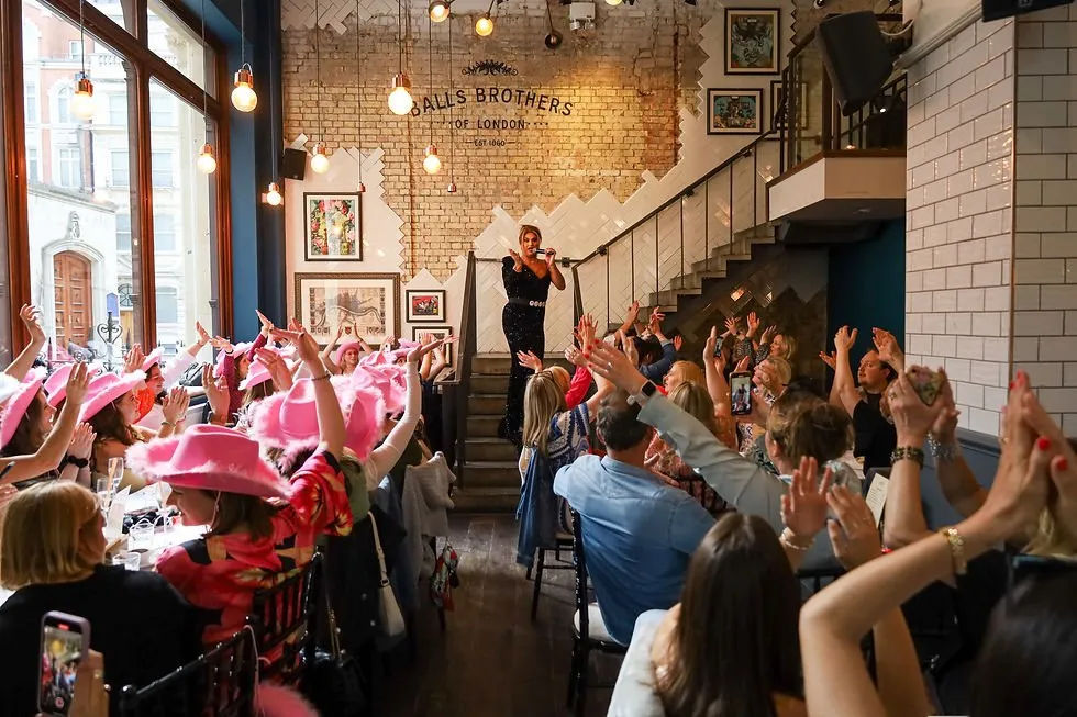 A drag performer sings on the staircase at Balls Brothers while the brunch crowd, some in pink cowboy hats, cheers