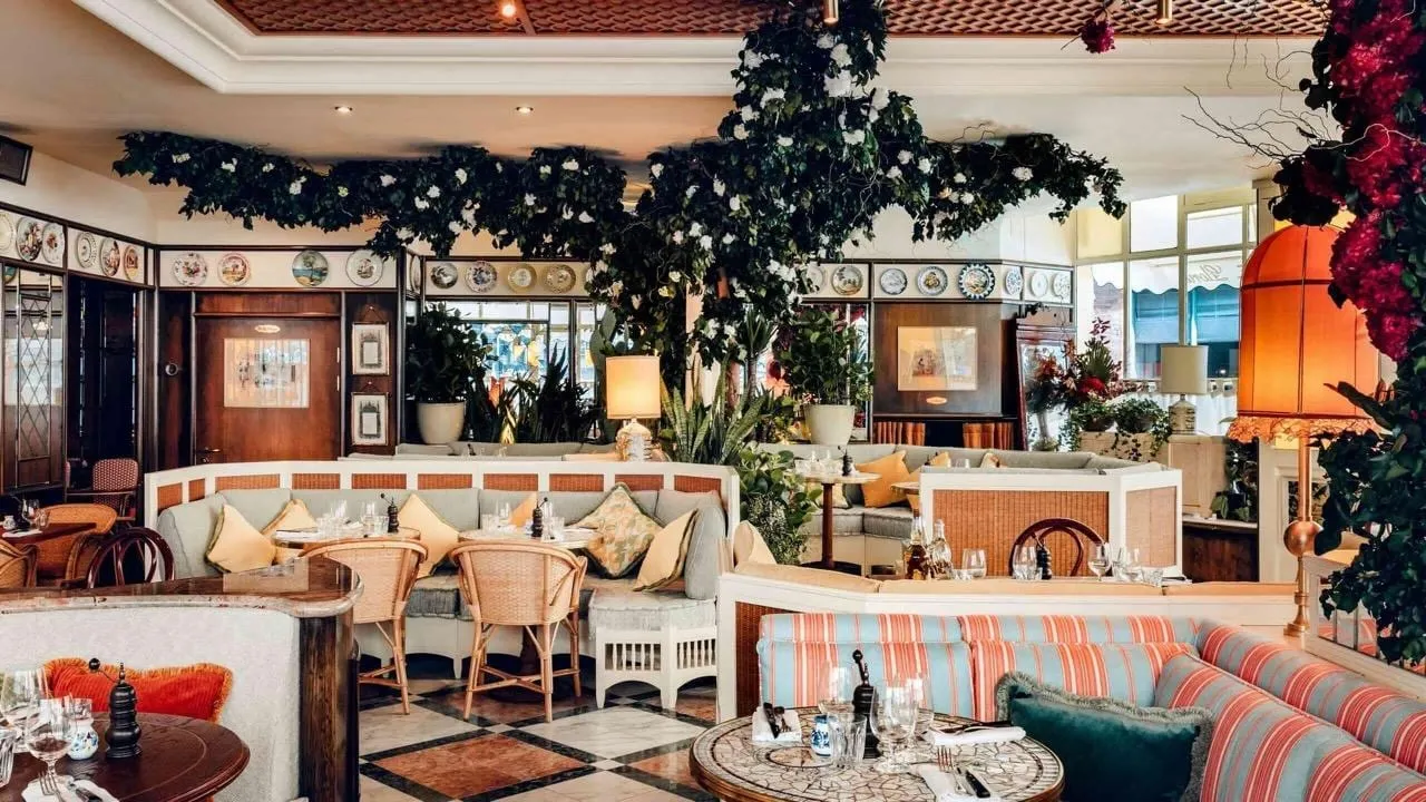 The ground-floor room at Gloria, a white-blossom tree spreading over striped banquettes and cane chairs, with hand-painted plates lining the walls