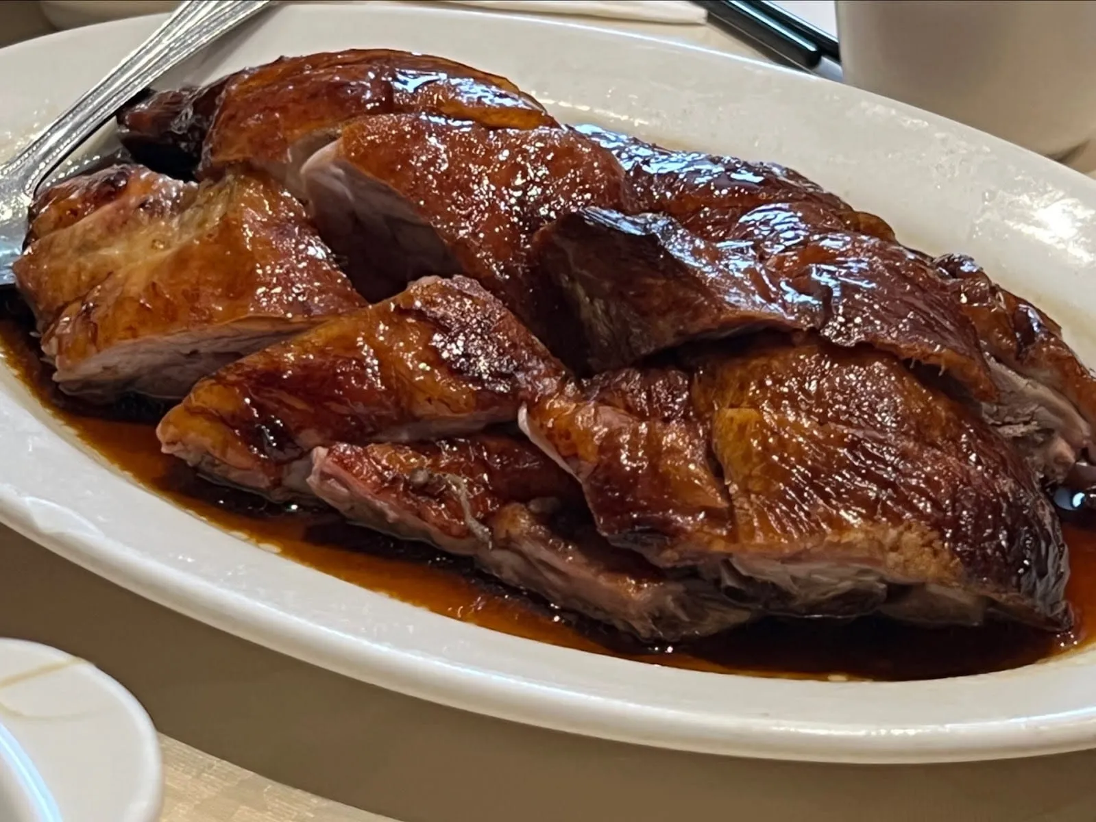 Sliced roast duck with dark lacquered skin, arranged on an oval white plate