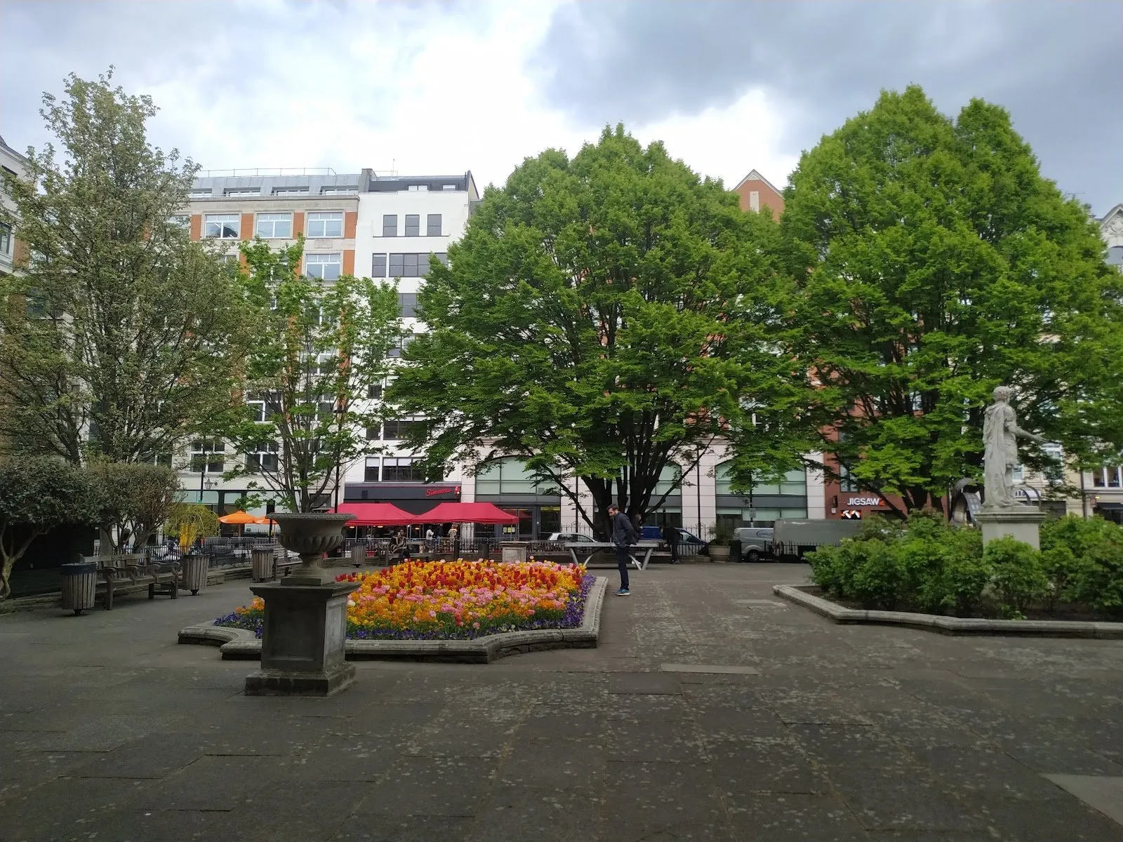 Golden Square's paved garden in spring: a bed of red, orange and pink tulips, a stone urn, large hornbeams behind, and the statue of George II on its plinth on the right