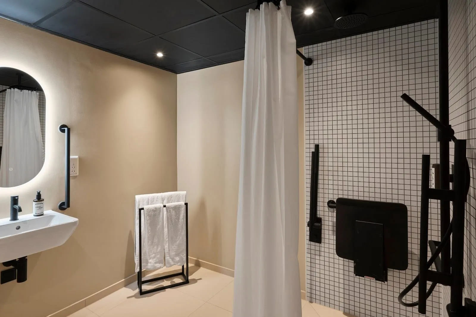 An accessible shower room at Good Hotel London with a basin, grab rails and a fold-down shower seat