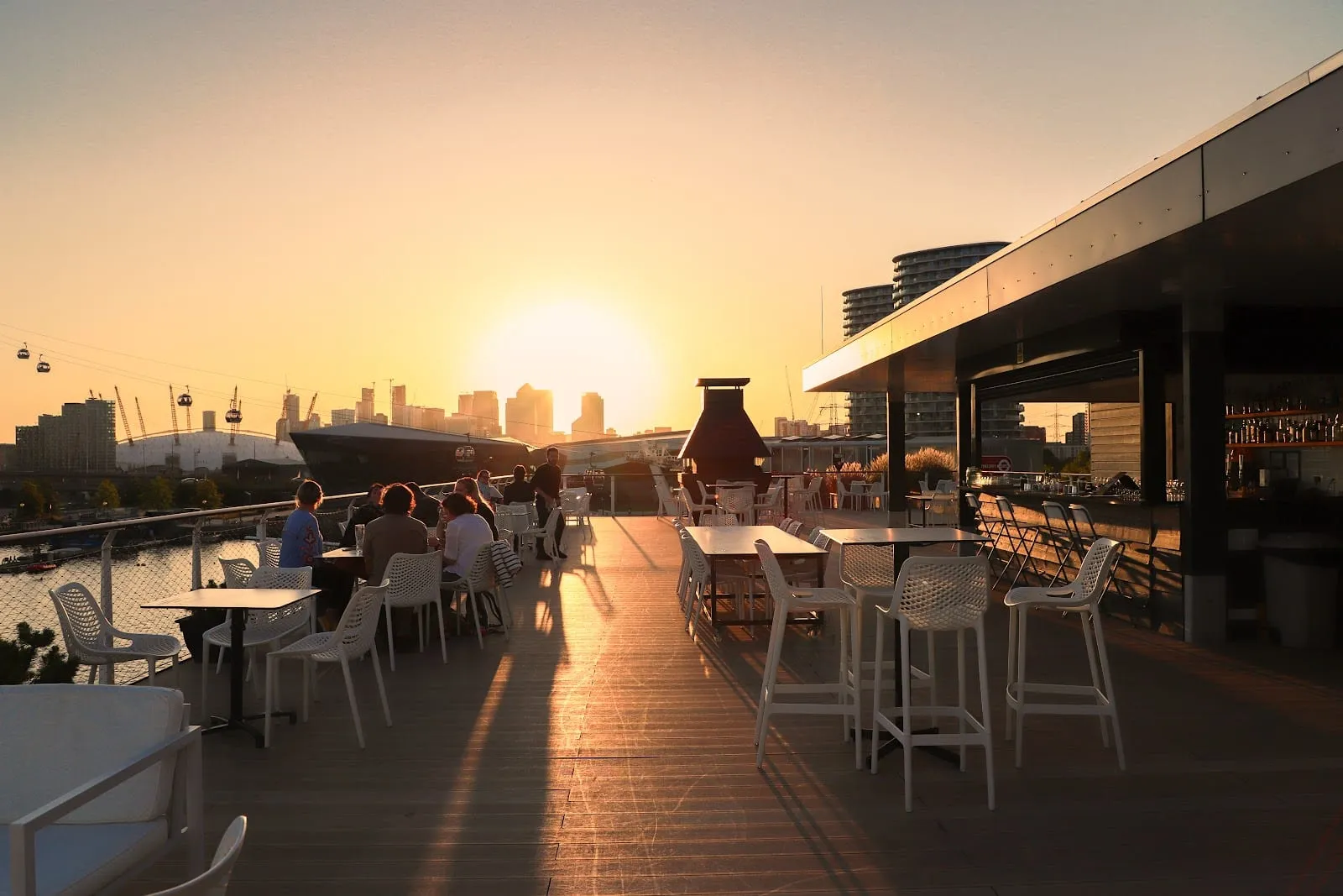 The roof terrace bar at Good Hotel London at sunset, with the O2 and the Canary Wharf towers across the water
